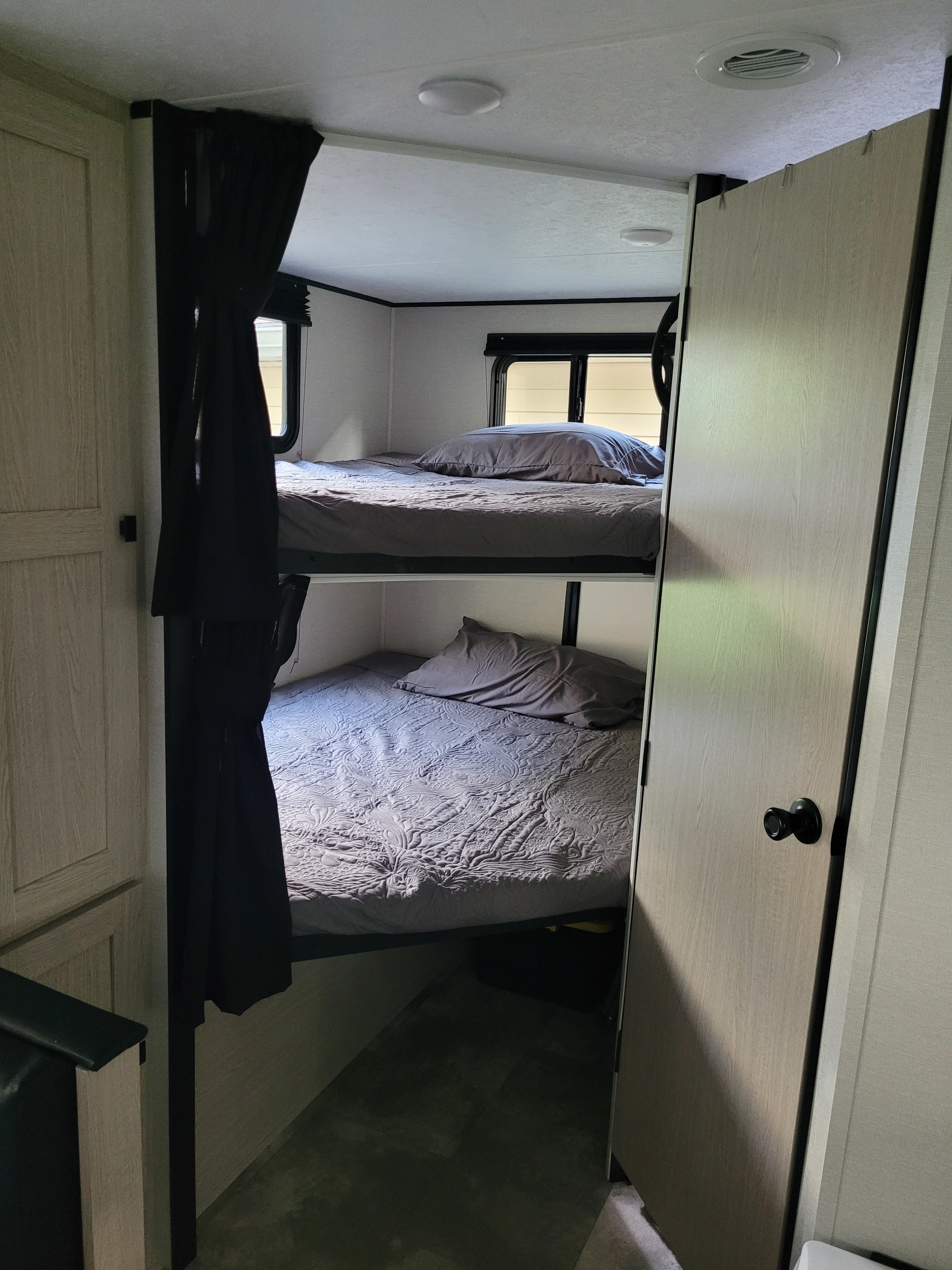 RV rental interior with dark curtains next to light wood and two bunk beds with grey bedding.. Coachmen Apex 2023