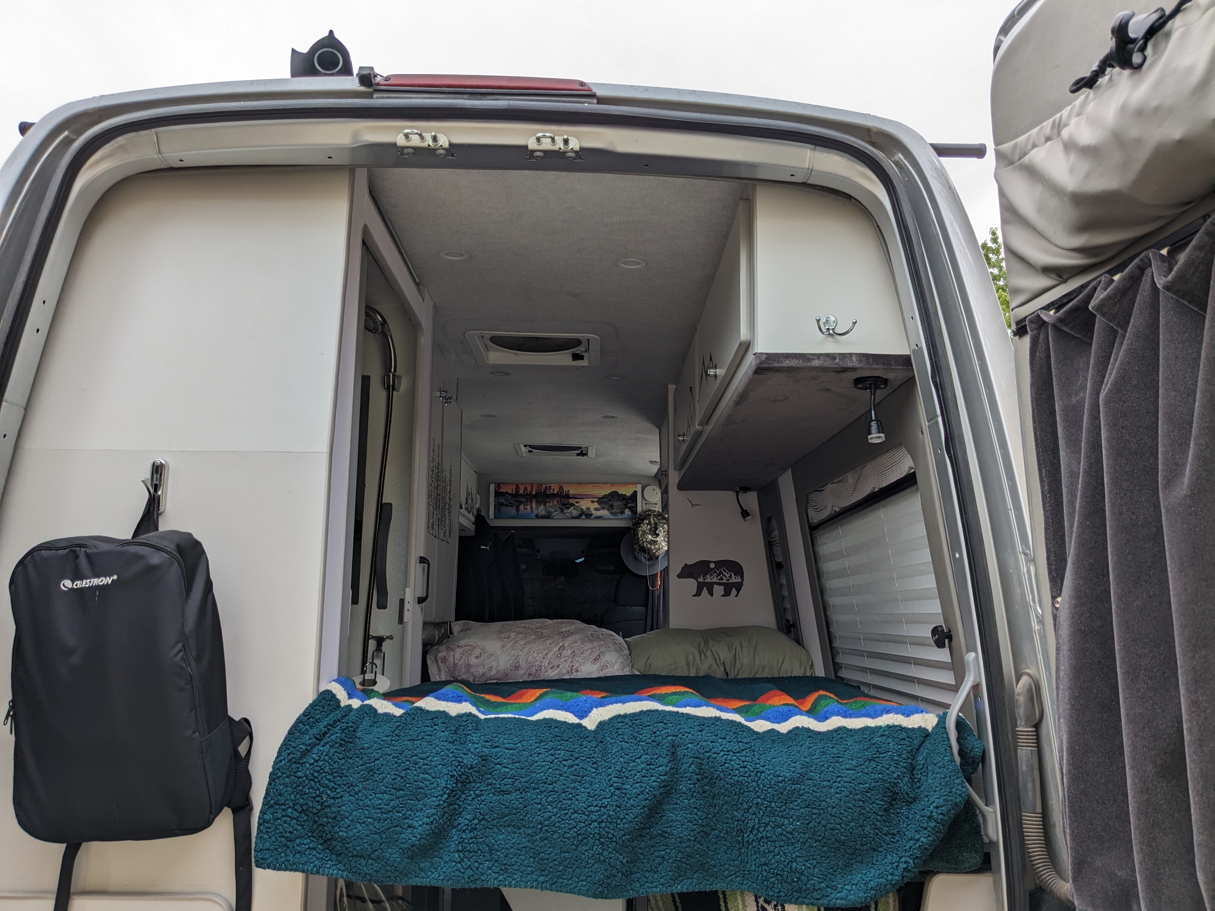 RV rental: Step inside this cozy camper van. Rear view showing a comfortable bed, storage, and shower for travel.. Sportsmobile Long Body 2013