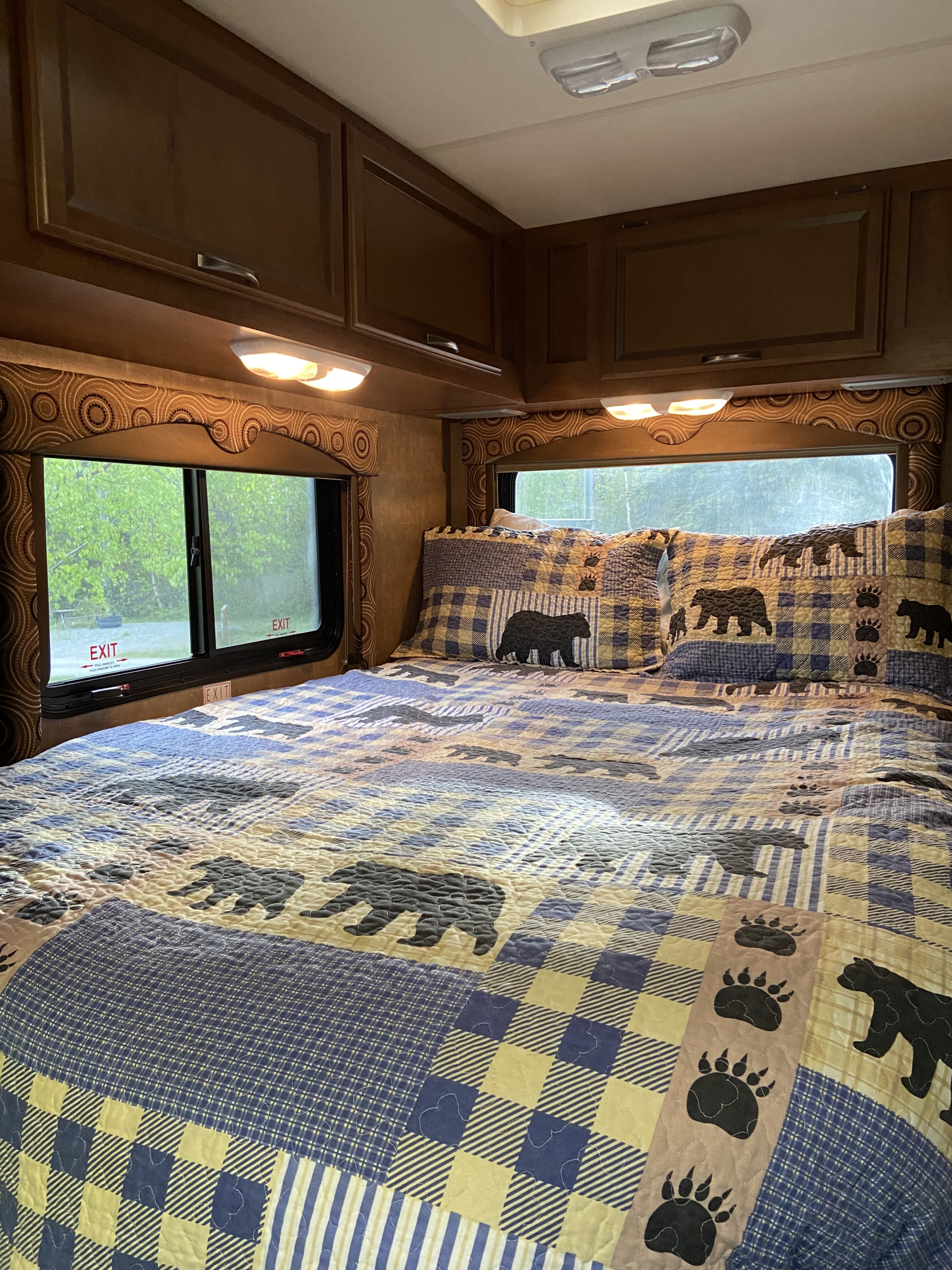Cozy RV rental bedroom featuring a blue and yellow bear-themed quilt, overhead storage, and windows showing outdoor greenery.. Thor Freedom Elite 2014