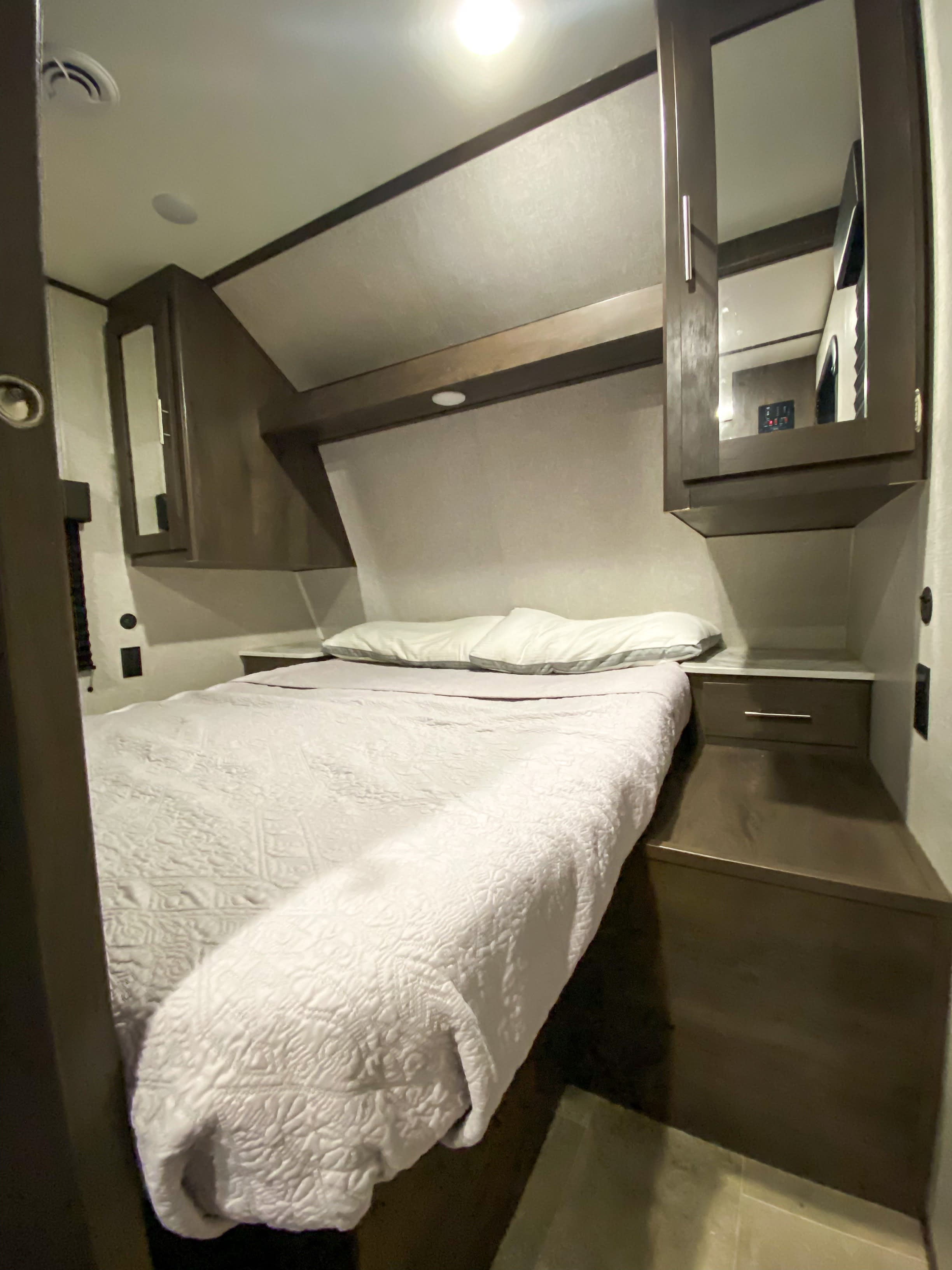Cozy RV rental bedroom with a comfortable bed, mirrored overhead cabinets, and built-in storage.. Dutchmen Coleman Lantern 2021