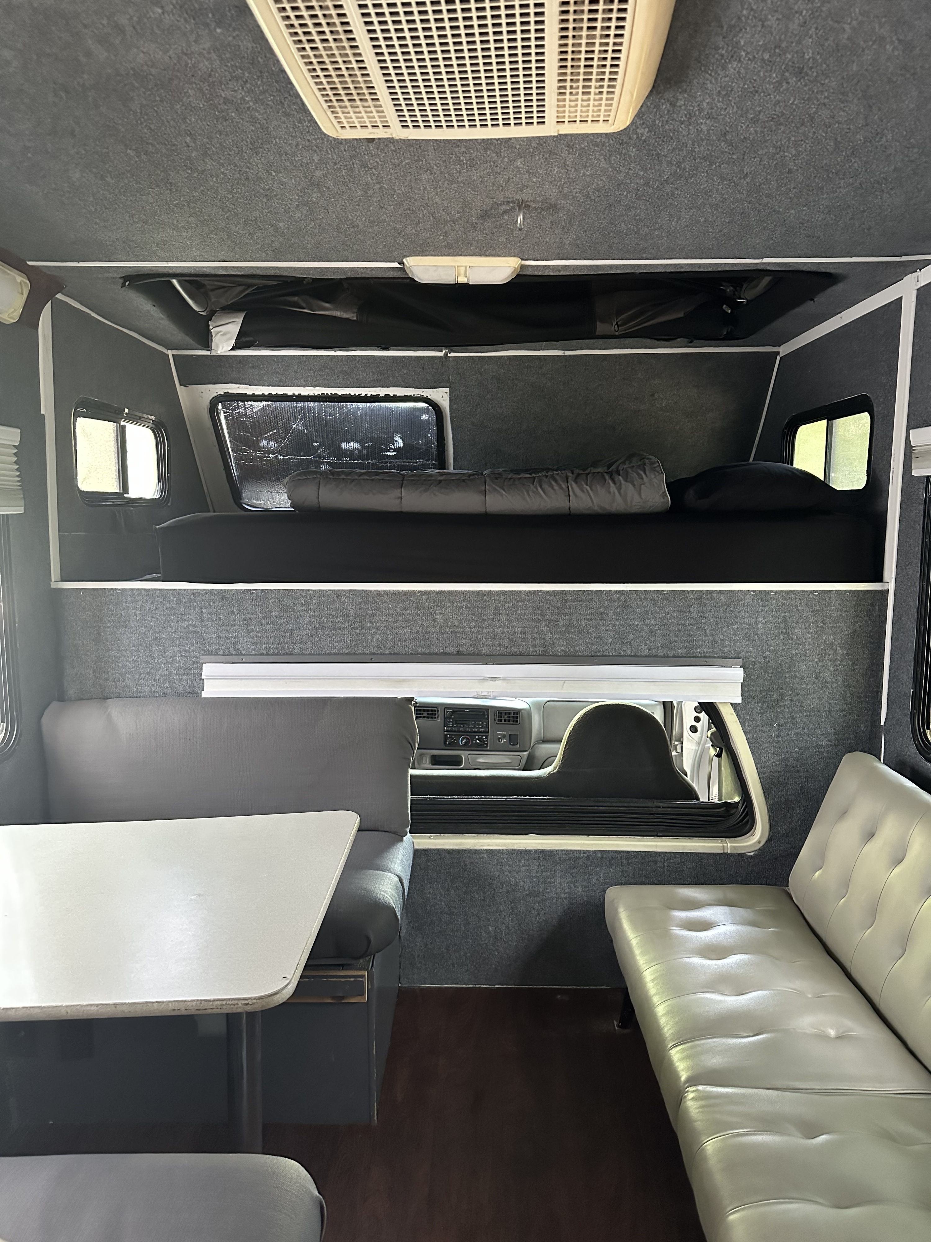 Cozy RV rental interior with an upper sleeping bunk, dinette area, and view of the front cab.. Four Winds Majestic 2004