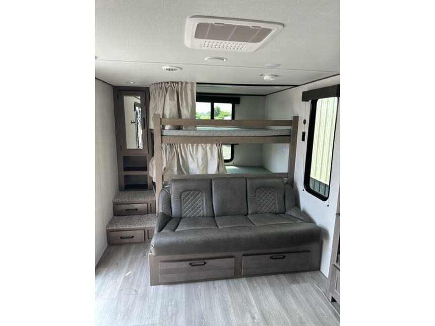 RV rental interior: bunk beds, a gray sofa with storage drawers, and steps leading to a raised area. Functional living space.. Grand Design Transcend Xplor 2021