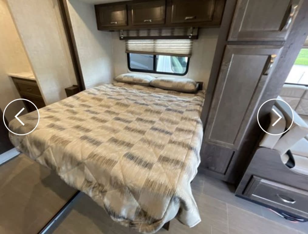 Explore this cozy RV rental's bedroom area with a comfy bed, overhead storage, and adjacent lounge seating.. Gulf Stream Conquest 2021