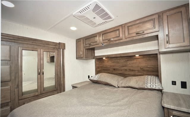 Spacious RV rental bedroom. Features a cozy bed, overhead wood cabinets, and large mirrored wardrobe for comfortable stays.. Forest River Sierra C-Class 2020