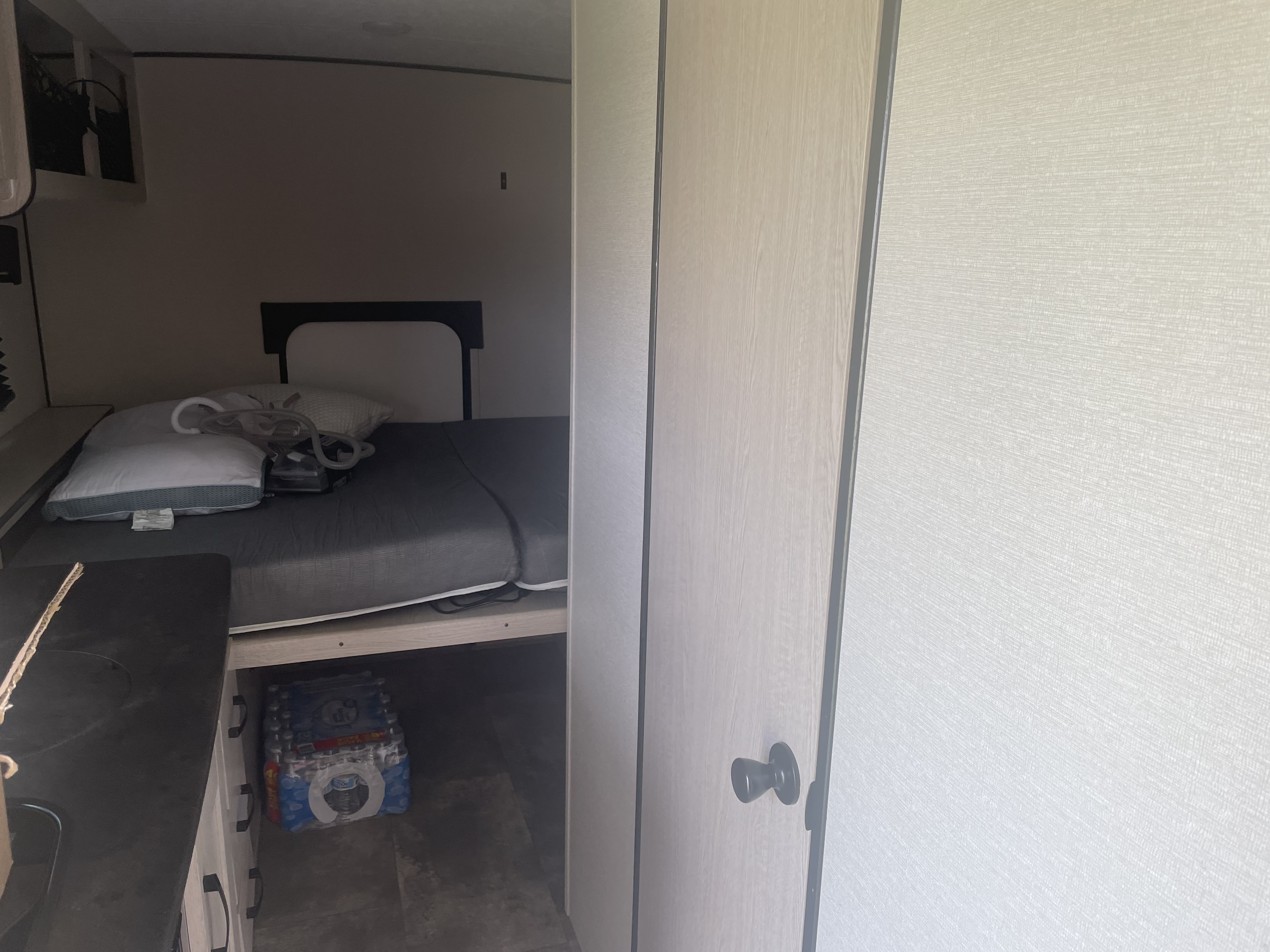 RV rental interior: A compact bedroom with a bed, CPAP machine, and cases of water stored underneath.. Coachmen Apex Remote 2022