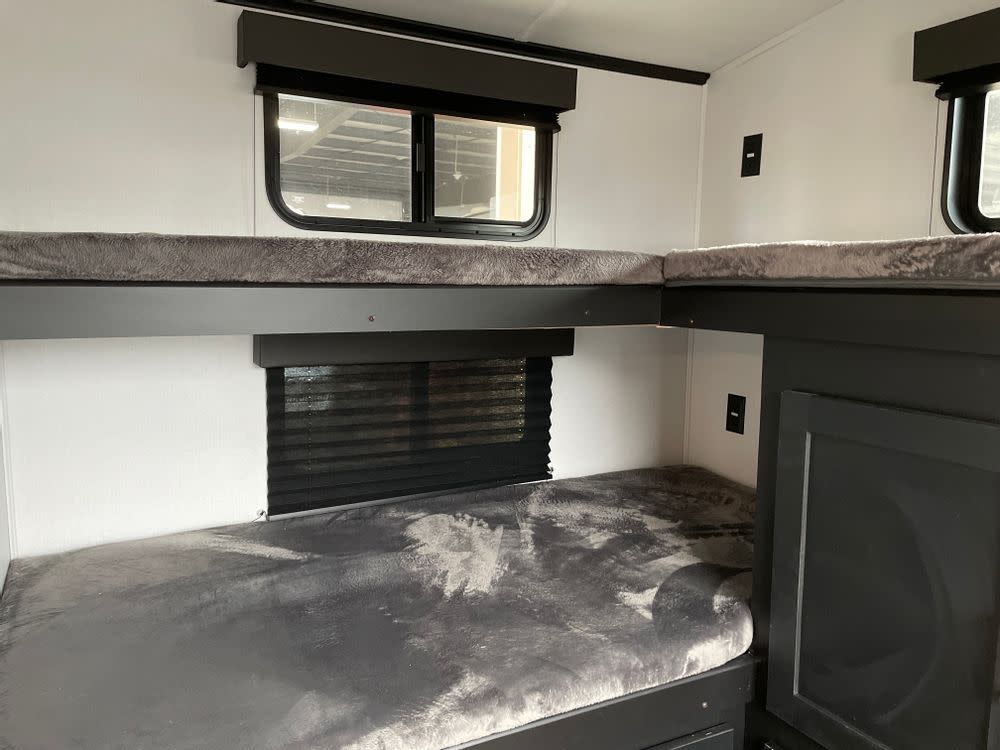 Explore this RV rental's cozy interior, featuring stacked bunk beds with plush grey bedding, windows, and charging outlets.. Keystone RV Outback Ultra-Lite 2022