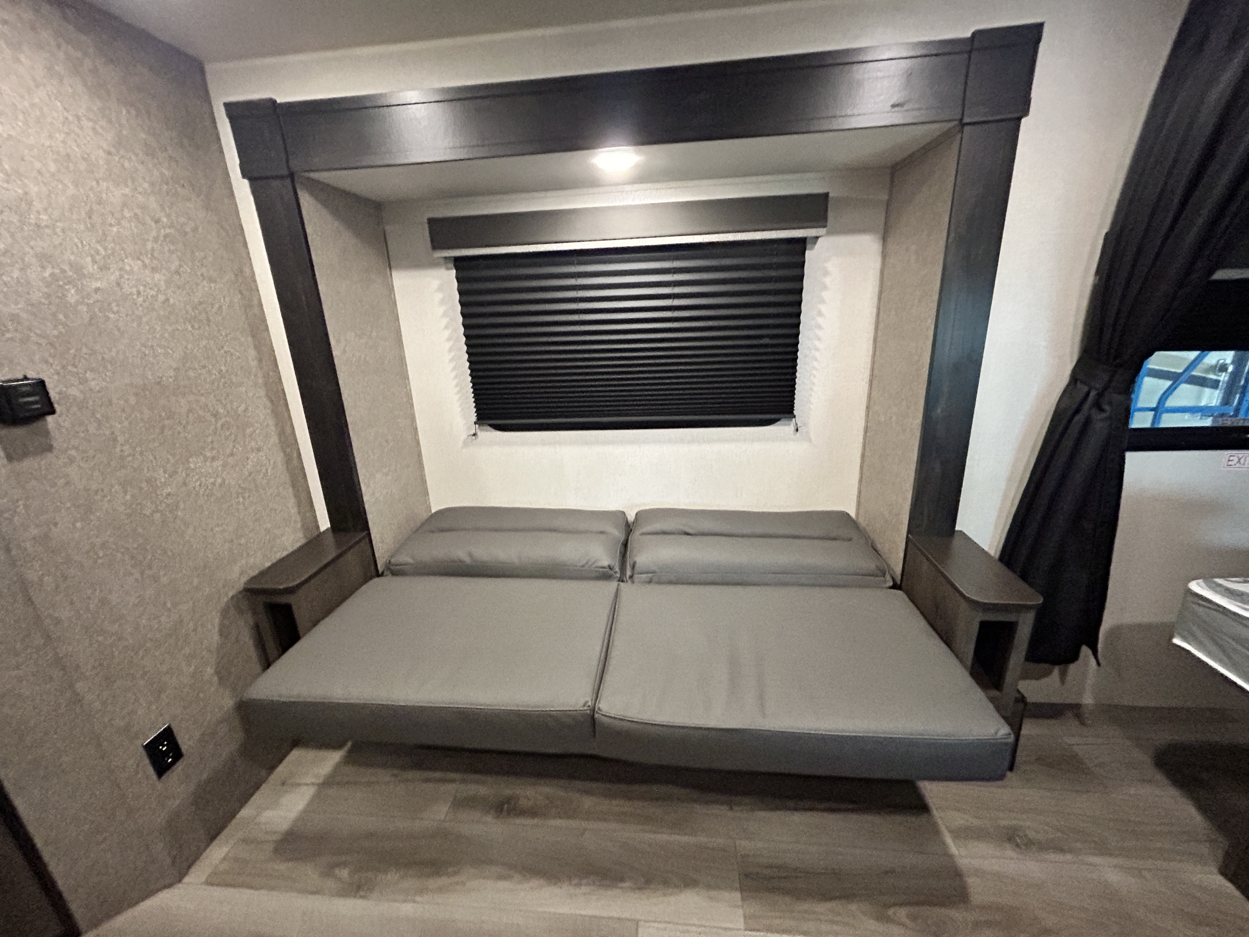An RV rental's versatile grey sofa bed, ideal for relaxing or sleeping, complemented by dark wood trim and window.. Starcraft Autumn Ridge 2021