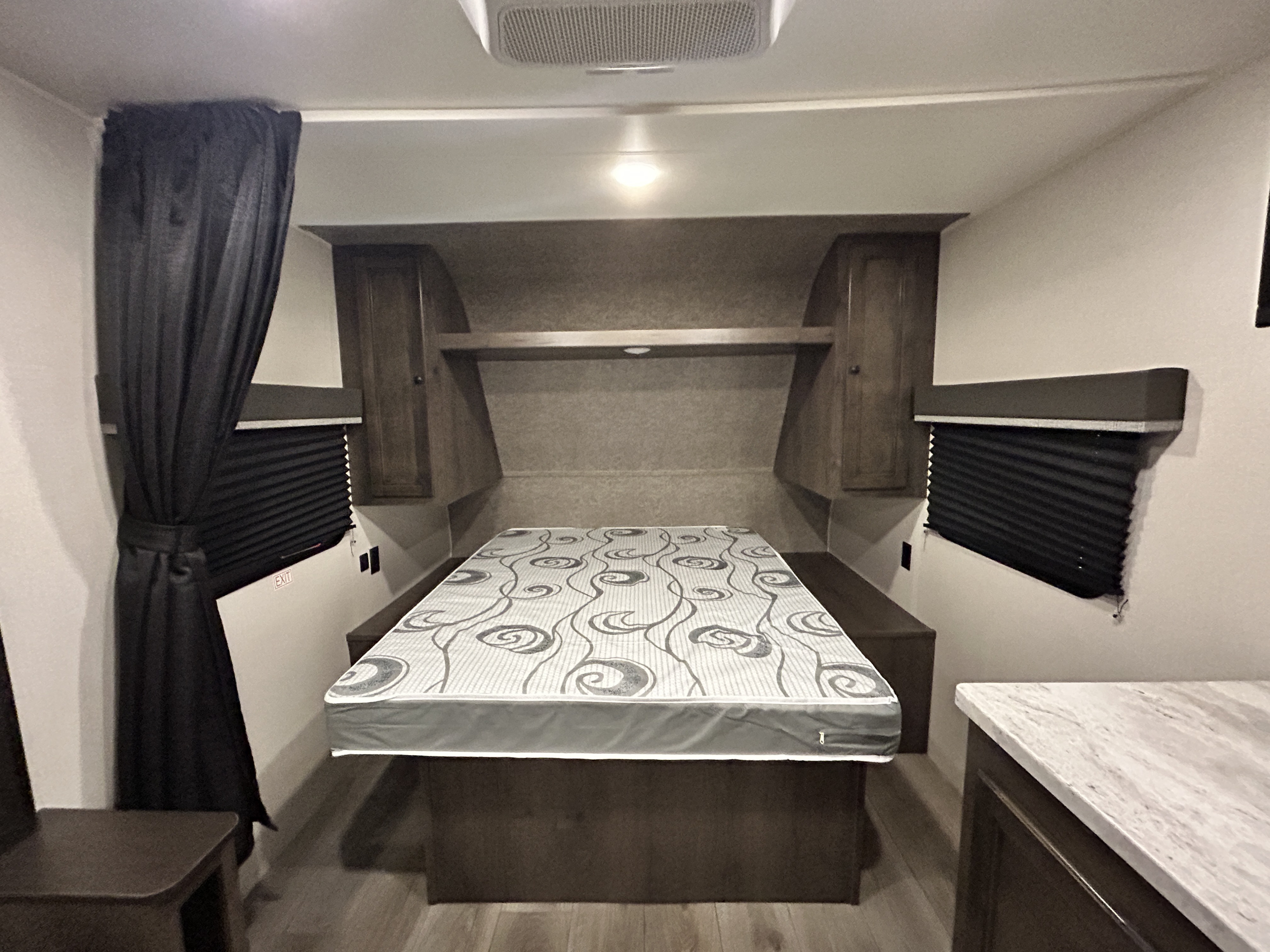 Inside an RV rental, a patterned mattress sits on a convertible bed base with side benches, flanked by cabinets and windows.. Starcraft Autumn Ridge 2021