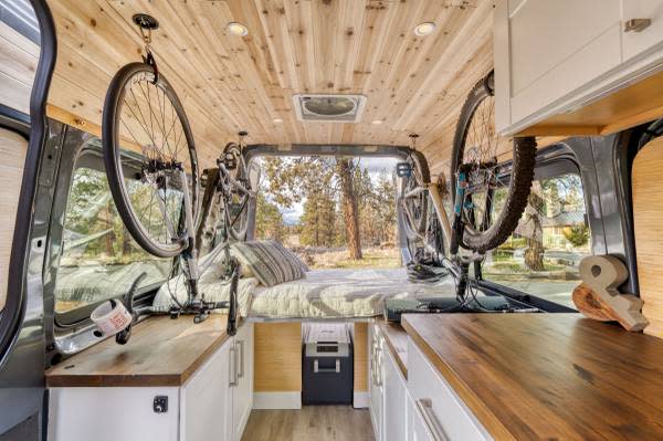 RV rental: Camper van interior featuring ceiling-mounted bikes, a bed, and functional wooden kitchen. Perfect for trips!. Mercedes-Benz Sprinter 2021