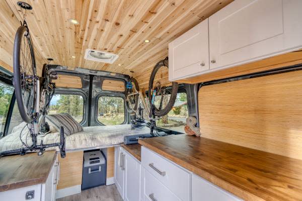 RV rental interior showcases clever storage for two bikes, a cozy bed, and functional kitchen with wooden accents.. Mercedes-Benz Sprinter 2021