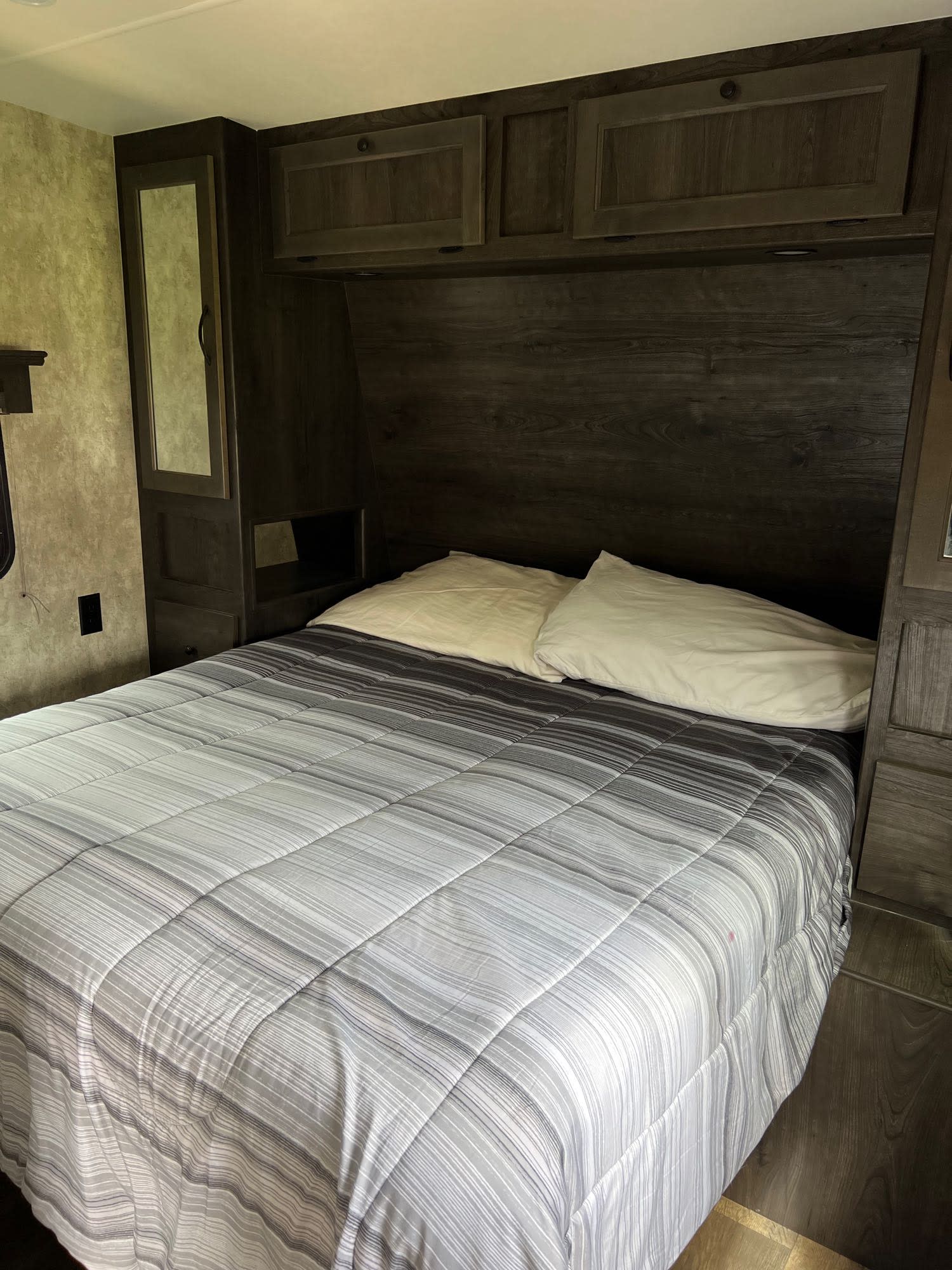 An RV rental bedroom showcasing a bed with a striped comforter, white pillows, and dark wood cabinetry.. Eclipse Recreational Vehicles Iconic 2018