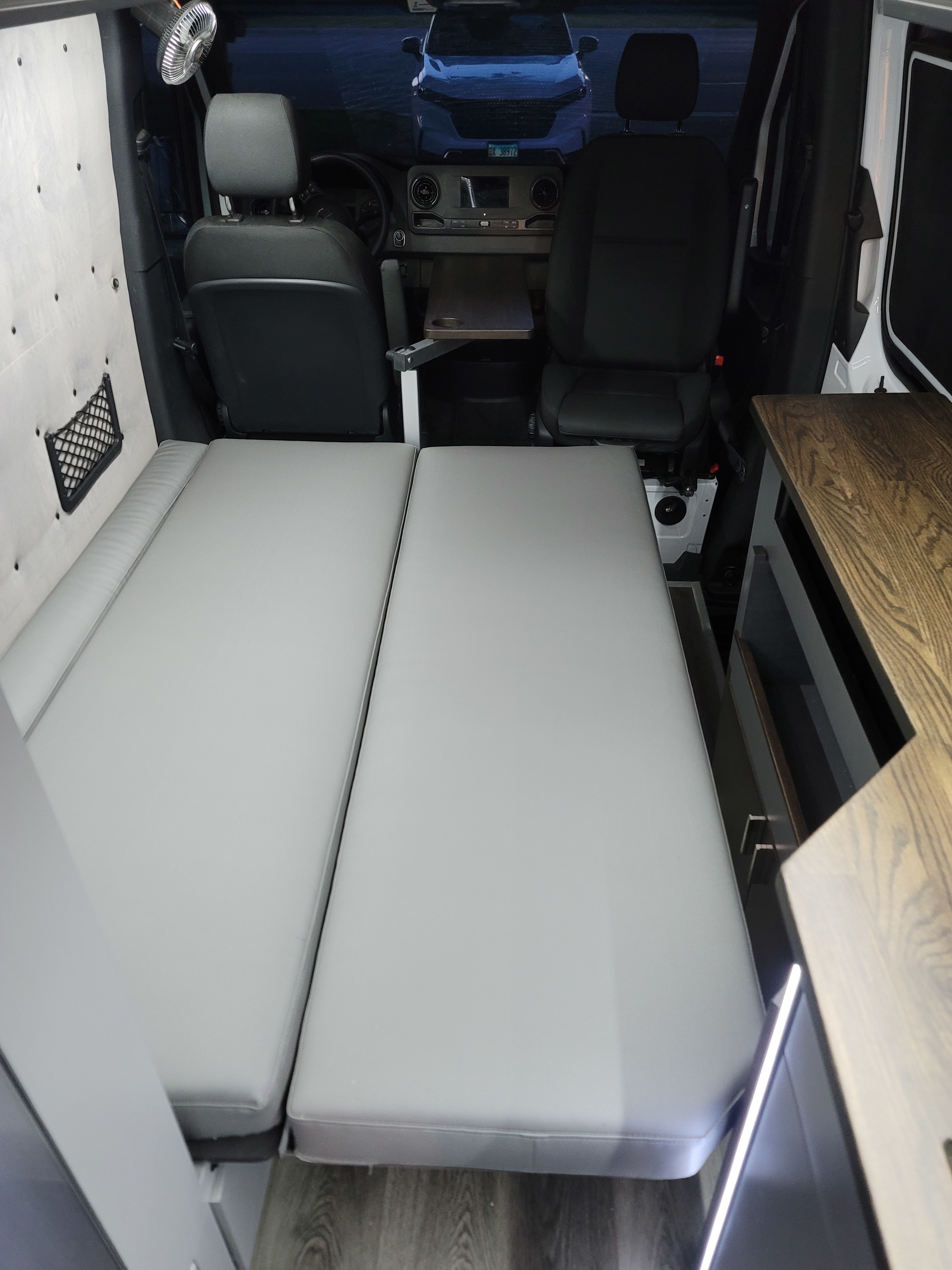 View from back: a cozy RV rental interior with a large bed, front swiveling seats, and a functional pull-out table.. Mercedes 2500 2022