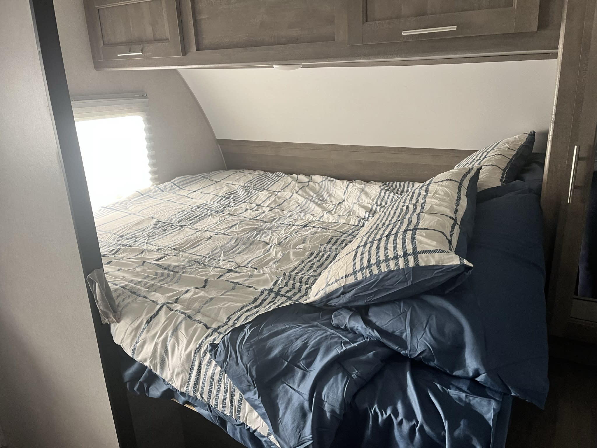 Cozy RV rental bedroom with striped bedding, overhead cabinets, and a window, offering a compact sleeping space.. Forest River XLR Micro Boost Toy Hauler 2020