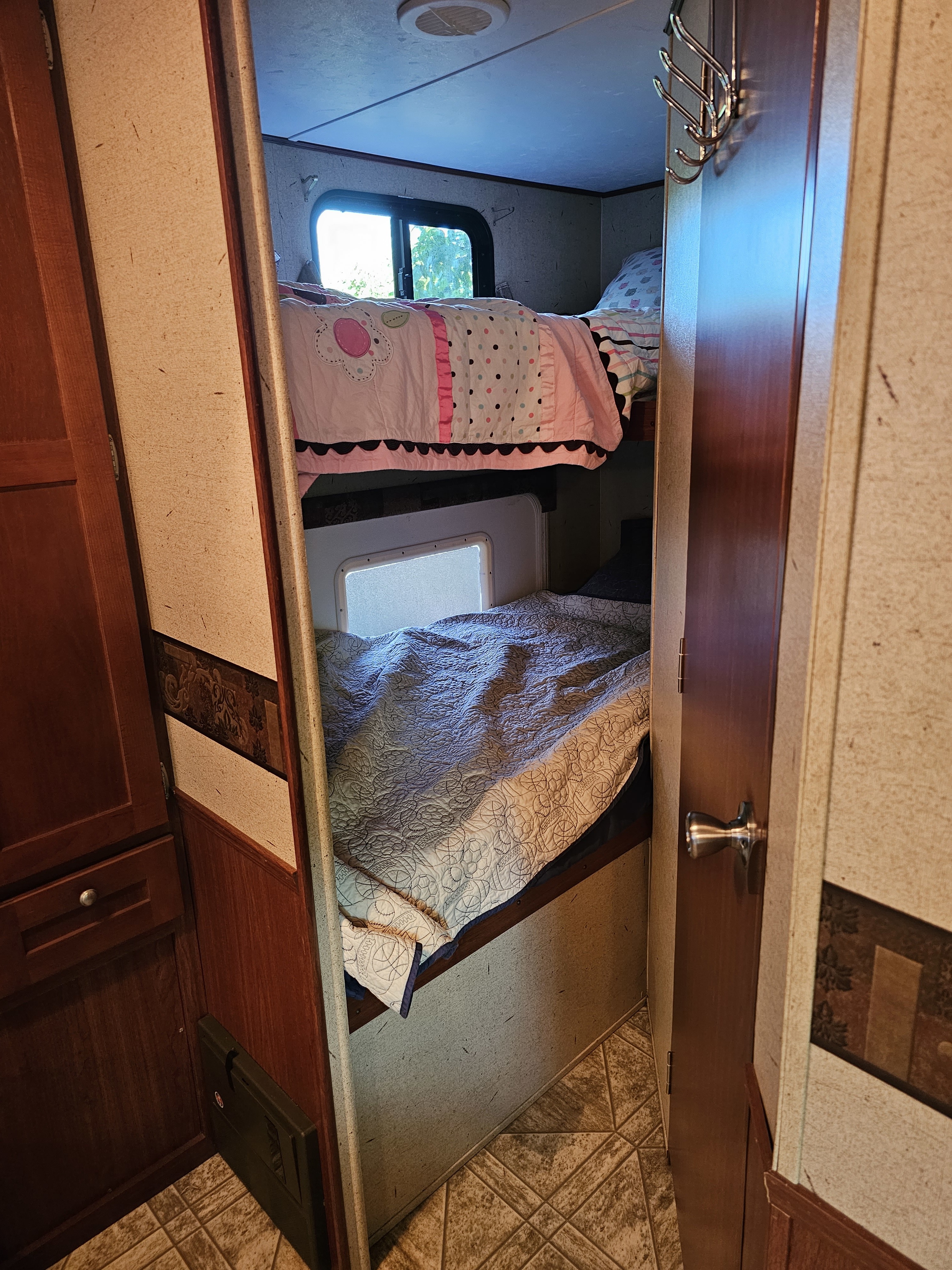 RV rental interior with cozy bunk beds: a top bed featuring pink bedding, and a bottom bed with gray quilting.. Crossroads RV Zinger 2010