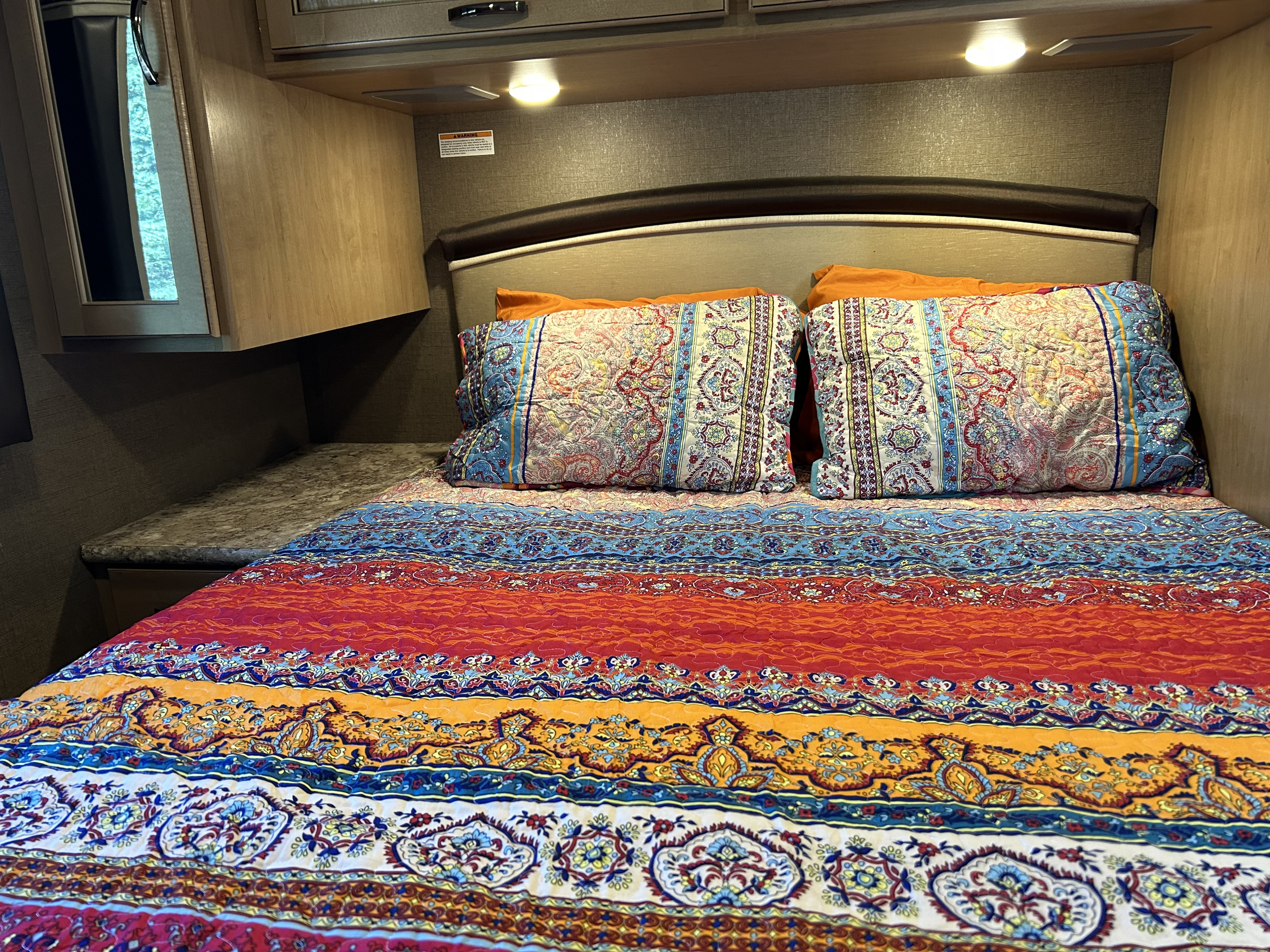 Vibrant RV rental bedroom features a comfy bed with colorful, patterned bedding and overhead storage.. Thor Chateau 2018