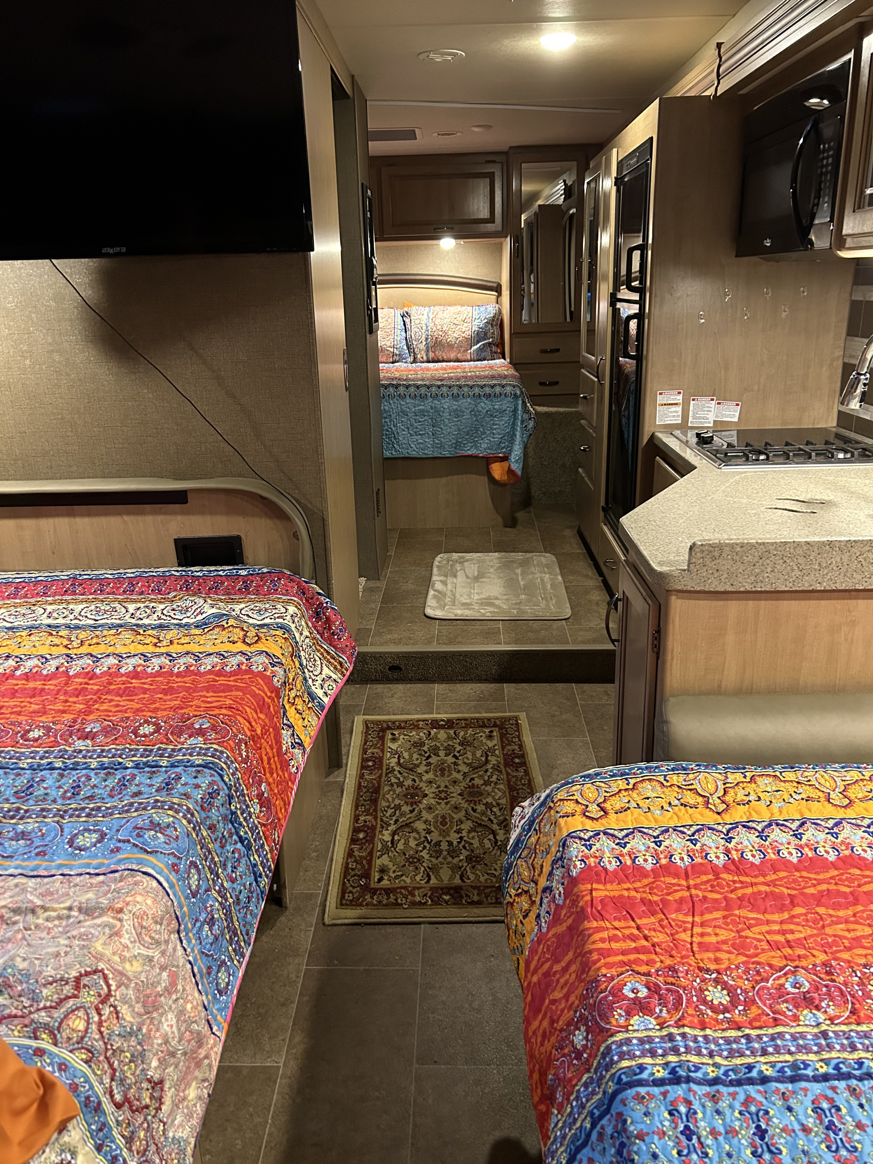 Inside a spacious RV rental, featuring colorful beds, a compact kitchen, and a TV for comfortable travel and living.. Thor Chateau 2018