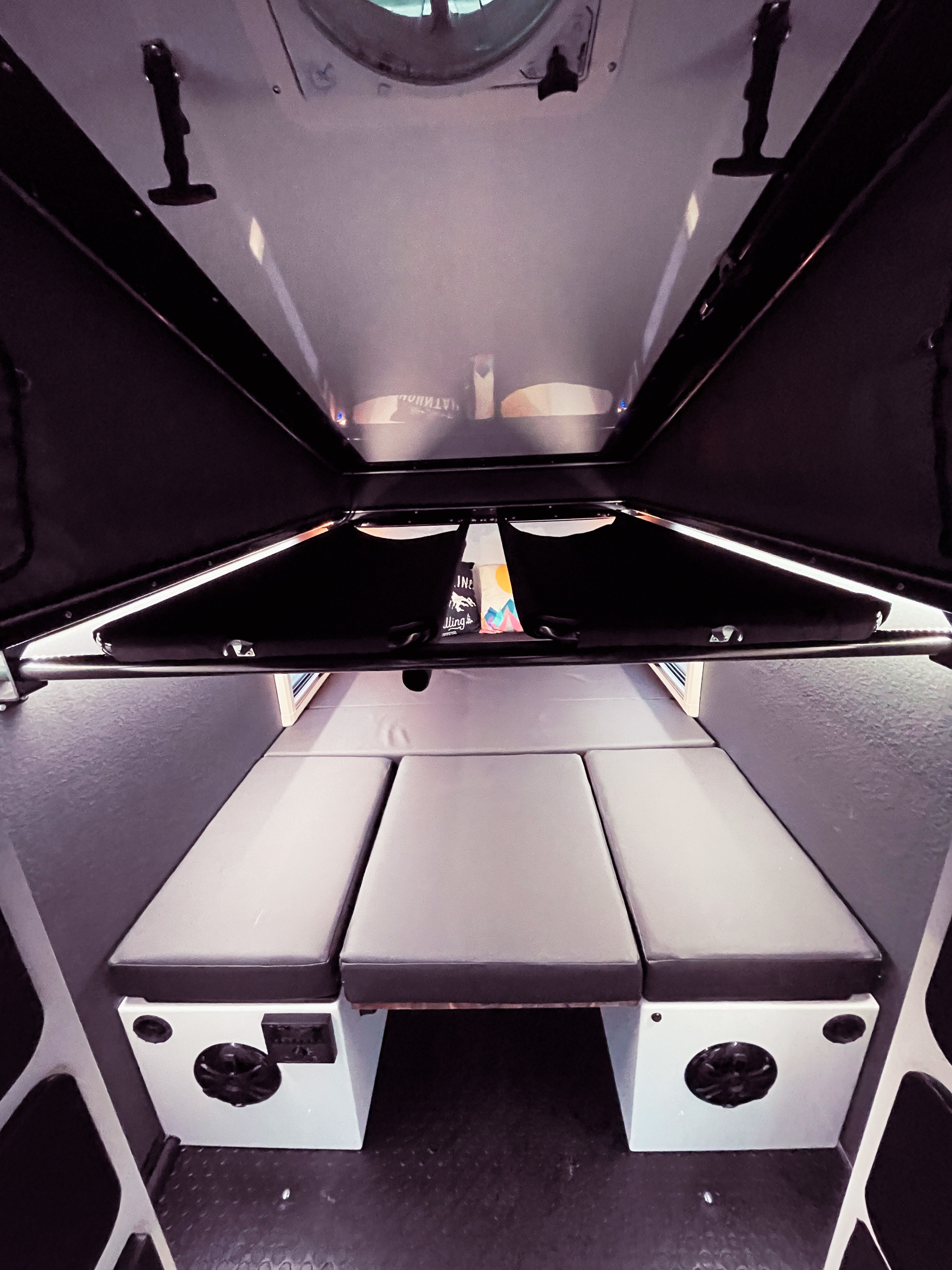Explore the compact RV rental interior, featuring a versatile sleeping area with three gray cushions and built-in amenities.. Mission Overland Summit 2022