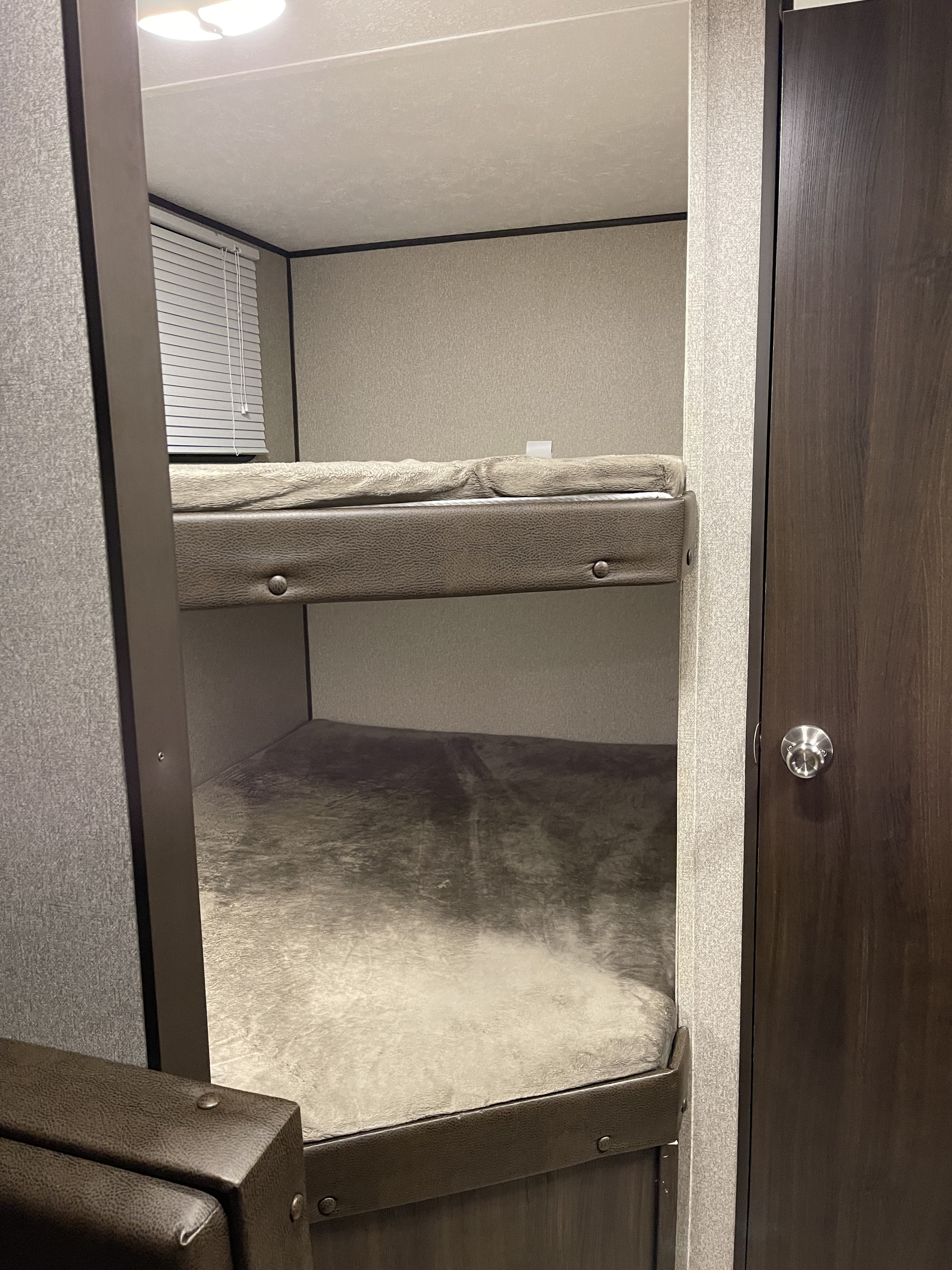 This RV rental interior features compact, cozy bunk beds with light textured walls, a window with blinds, and dark wood accents.. Keystone RV Springdale 2018