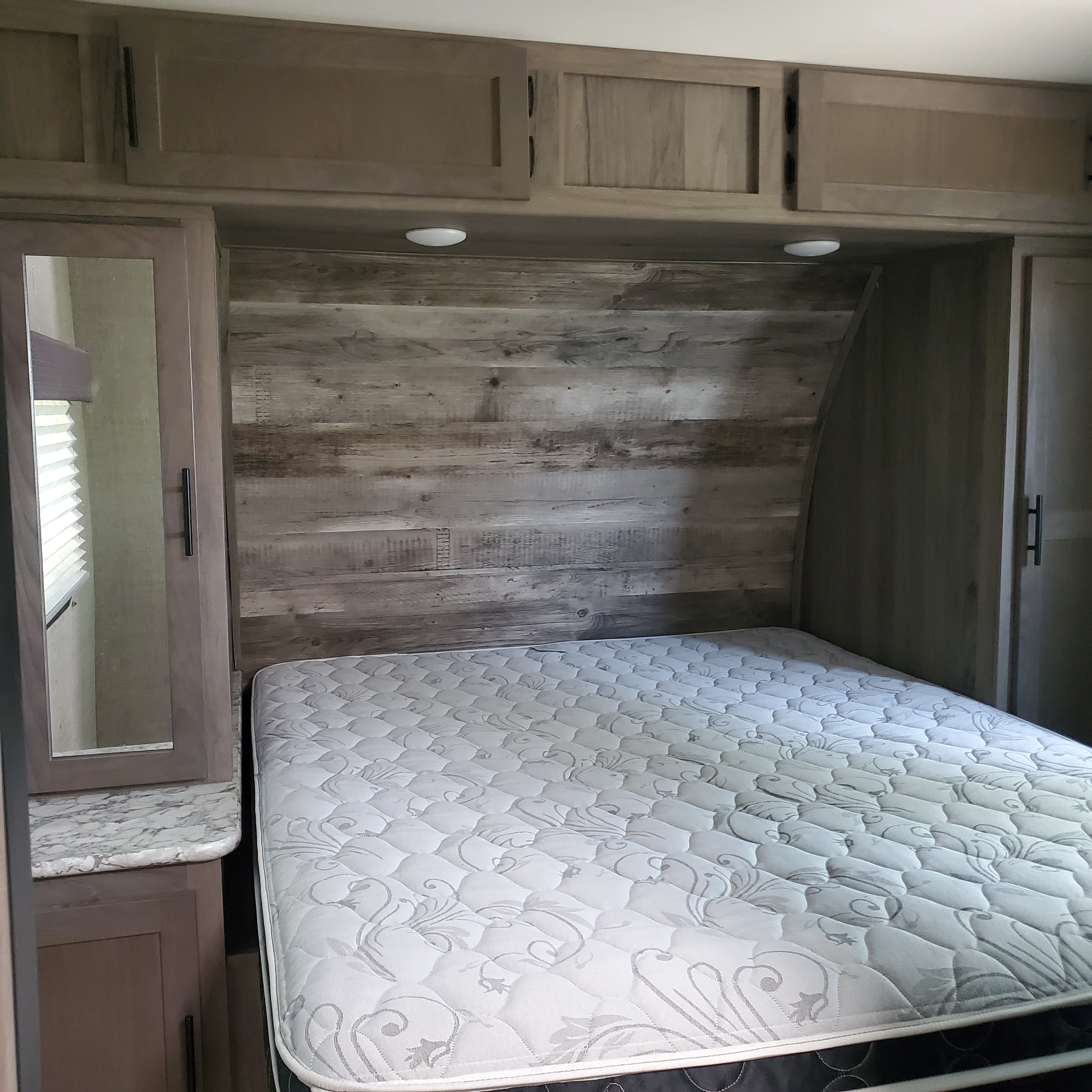 This cozy RV rental bedroom features a comfy bed, wood-paneled wall, overhead cabinets, and mirrored storage.. Gulf Stream Conquest Supreme 2021