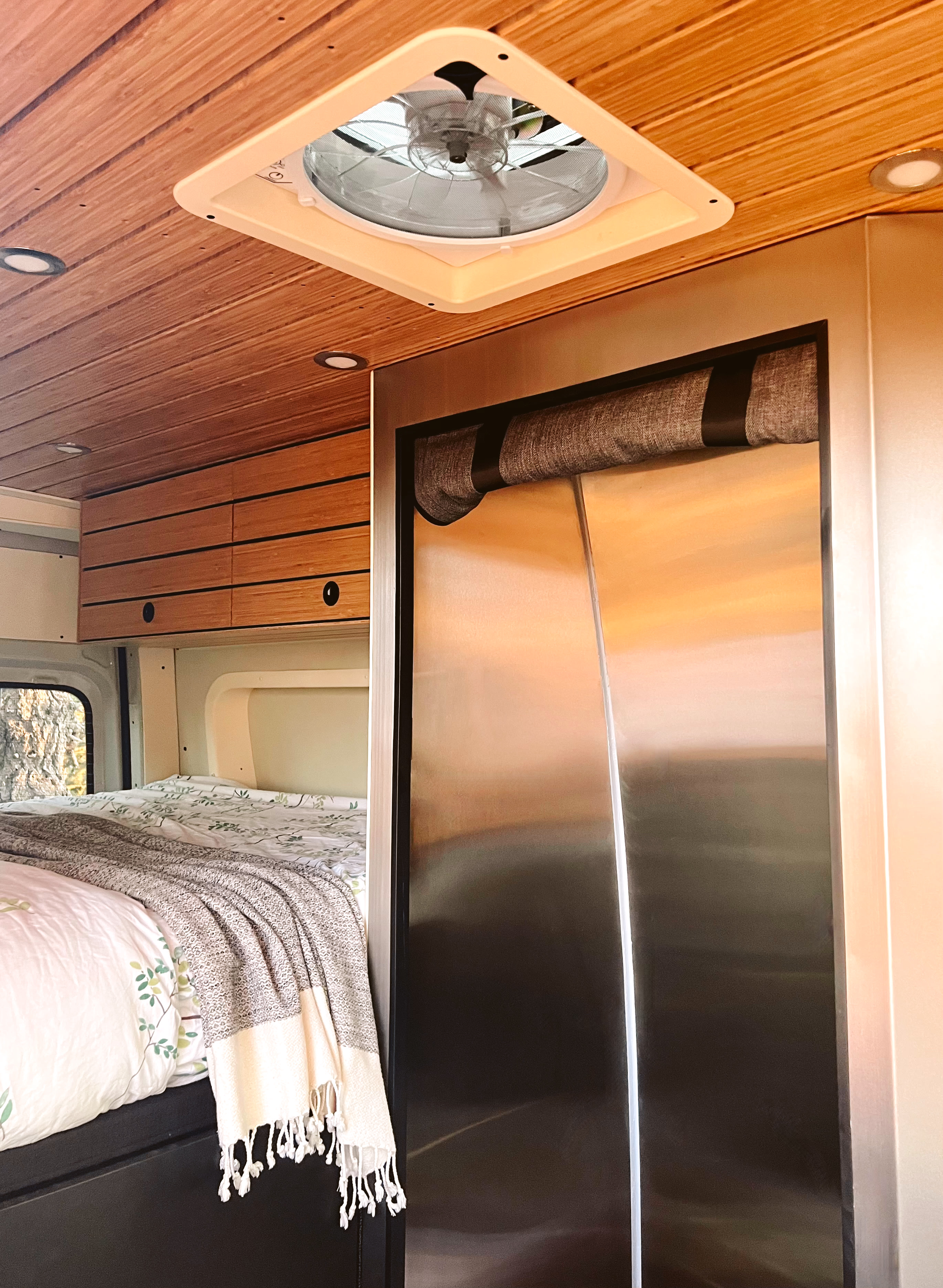 Modern rv rental interior with wood ceiling, fan, cabinets, cozy bed, and large stainless-steel refrigerator.. Mercedes-Benz Sprinter 2023