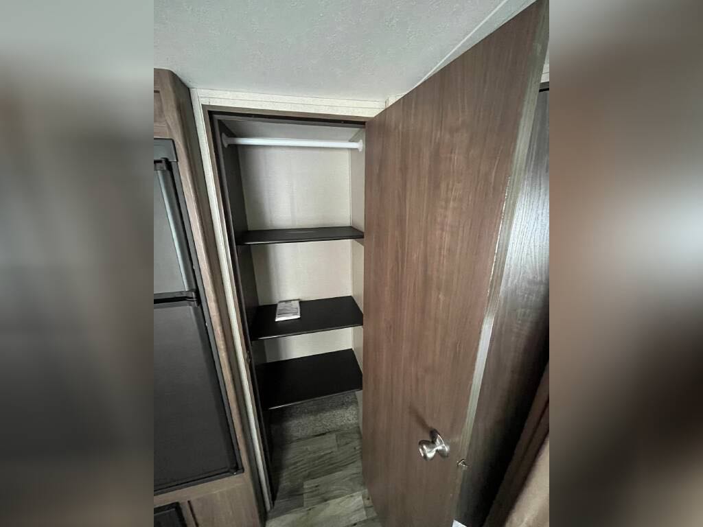 Spacious RV rental wardrobe with hanging rod and three shelves, perfect for organized storage. Refrigerator visible left.. Keystone Hideout 2017