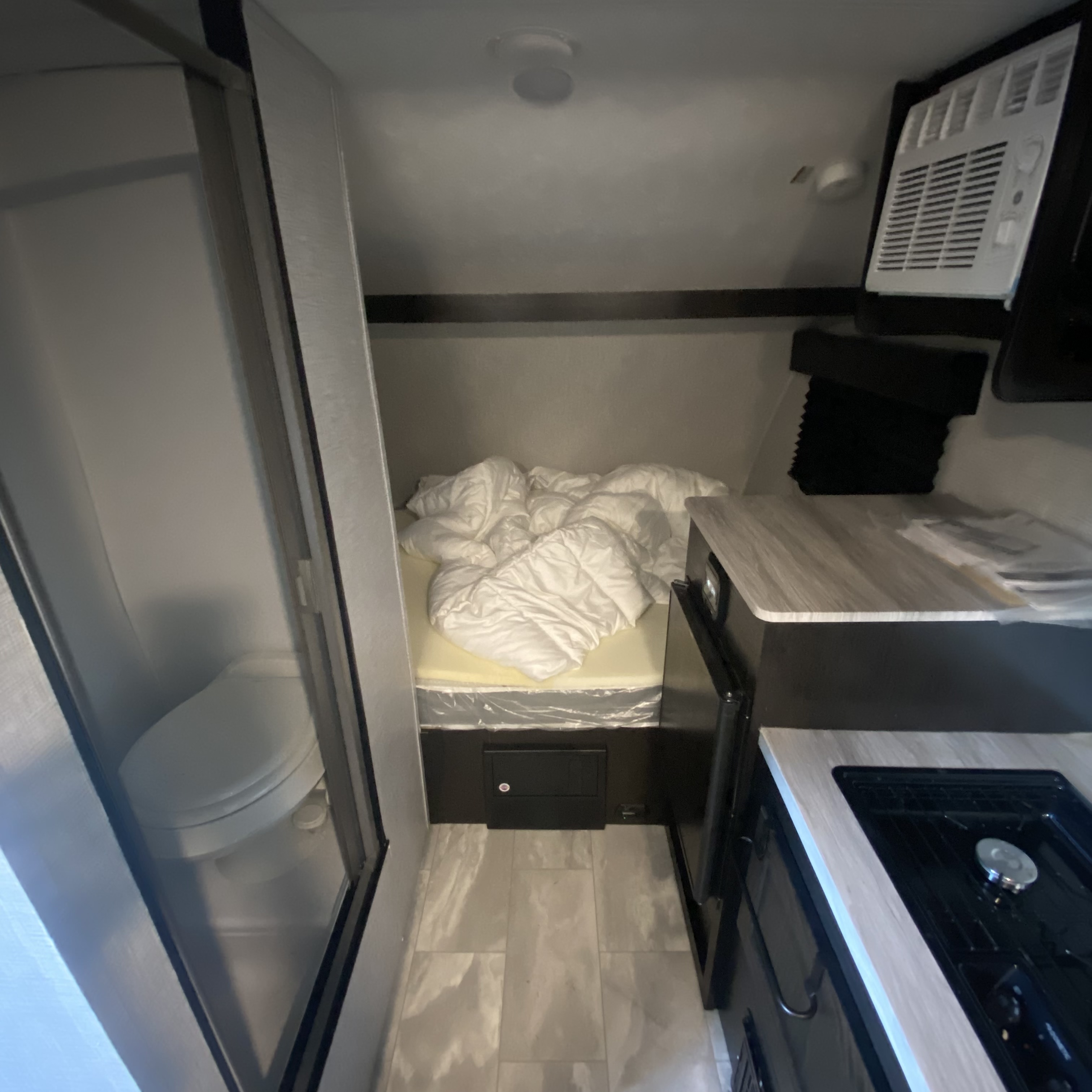 Cozy RV rental interior: featuring a compact kitchen, bed with protective wrap, and a shower/toilet bathroom on the left.. Braxton Creek Free Solo 2021