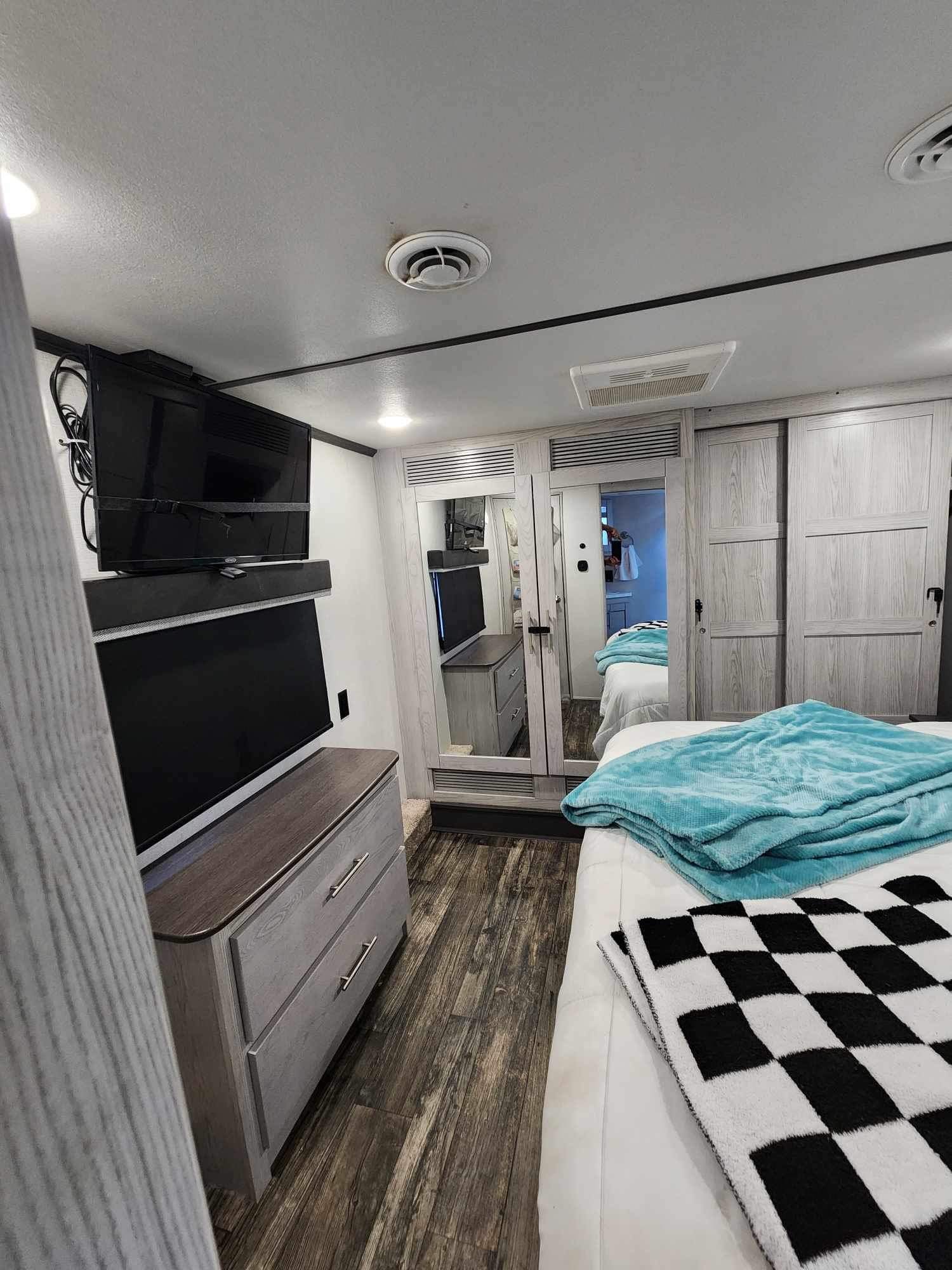 Explore this modern RV rental bedroom: a comfortable bed with teal blanket, ample storage with mirrored closets, and entertainment TVs.. Keystone RV Fuzion Toy Hauler 2021