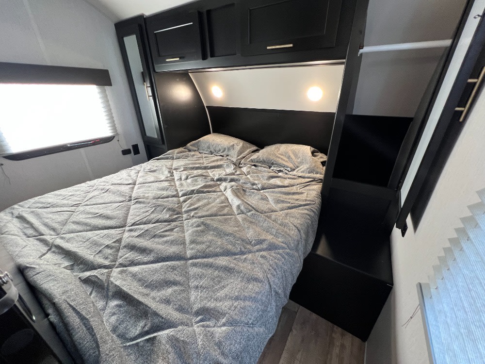 Modern RV rental bedroom features a comfy grey bed, black cabinets & illuminated headboard. Perfect for road trips.. Forest River Cherokee Grey Wolf 2023