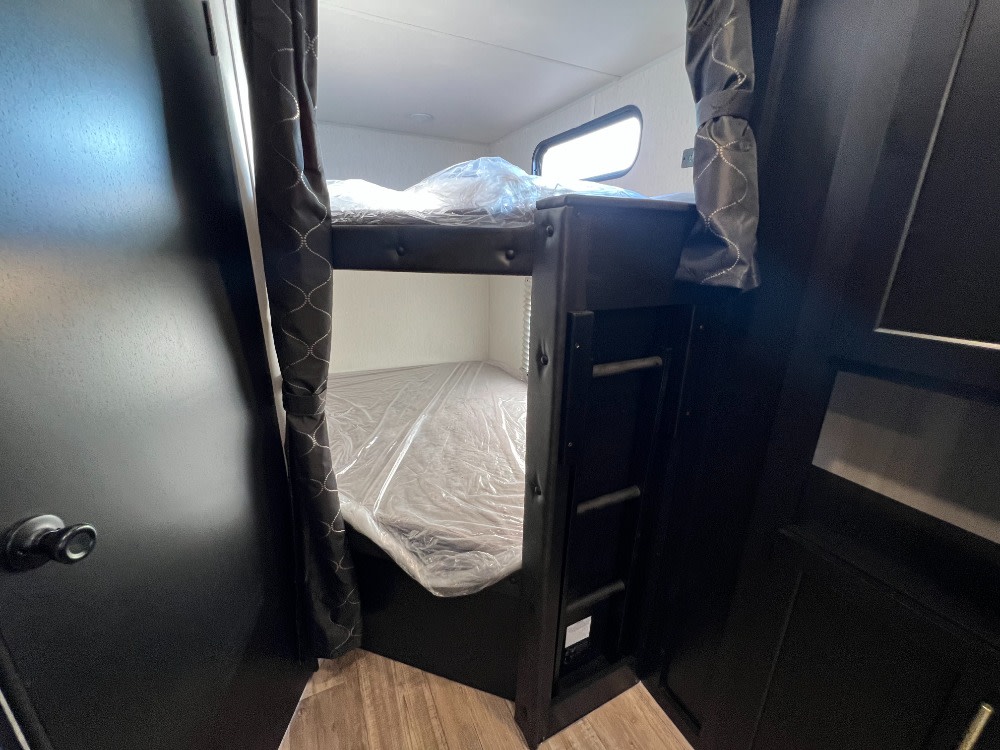 RV rental interior featuring dark-toned bunk beds, a ladder, and mattresses covered for readiness.. Forest River Cherokee Grey Wolf 2023