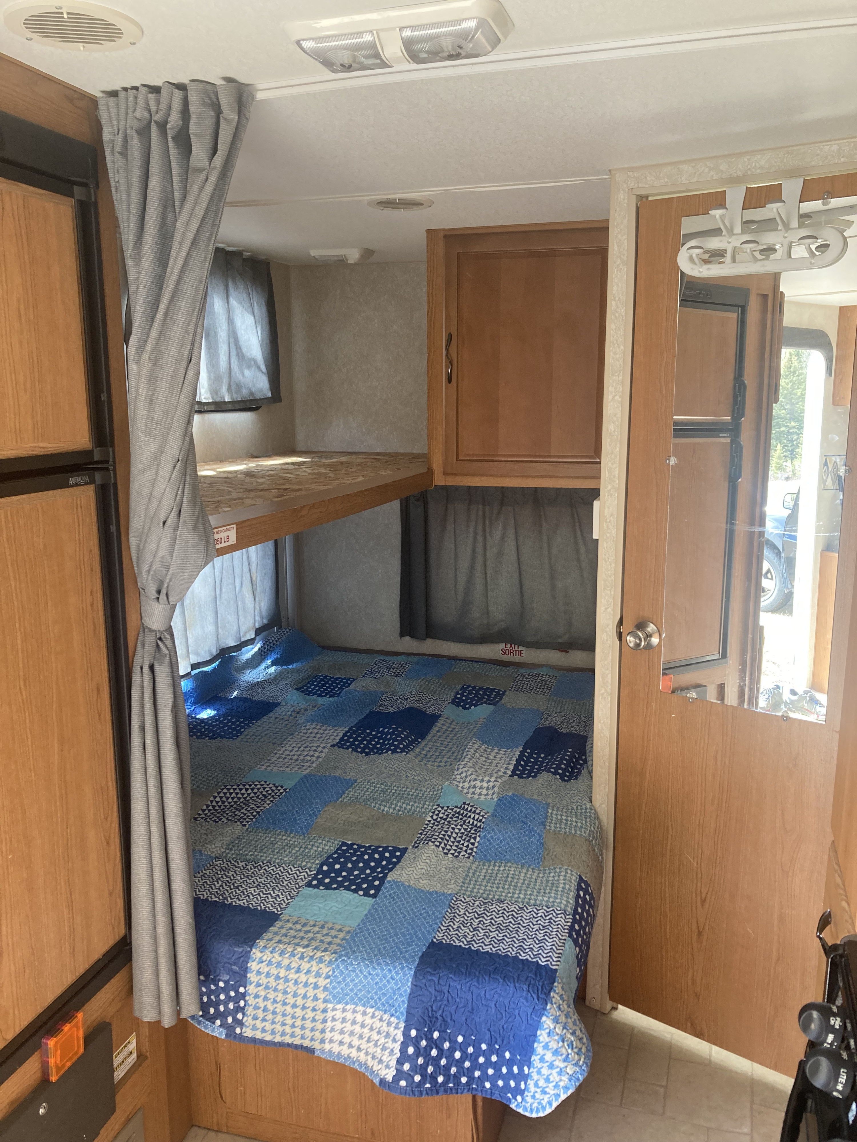 RV rental bunk beds with blue quilt, adjacent to refrigerator and a mirrored door. Compact sleeping in this RV interior.. Fleetwood RB220 2004