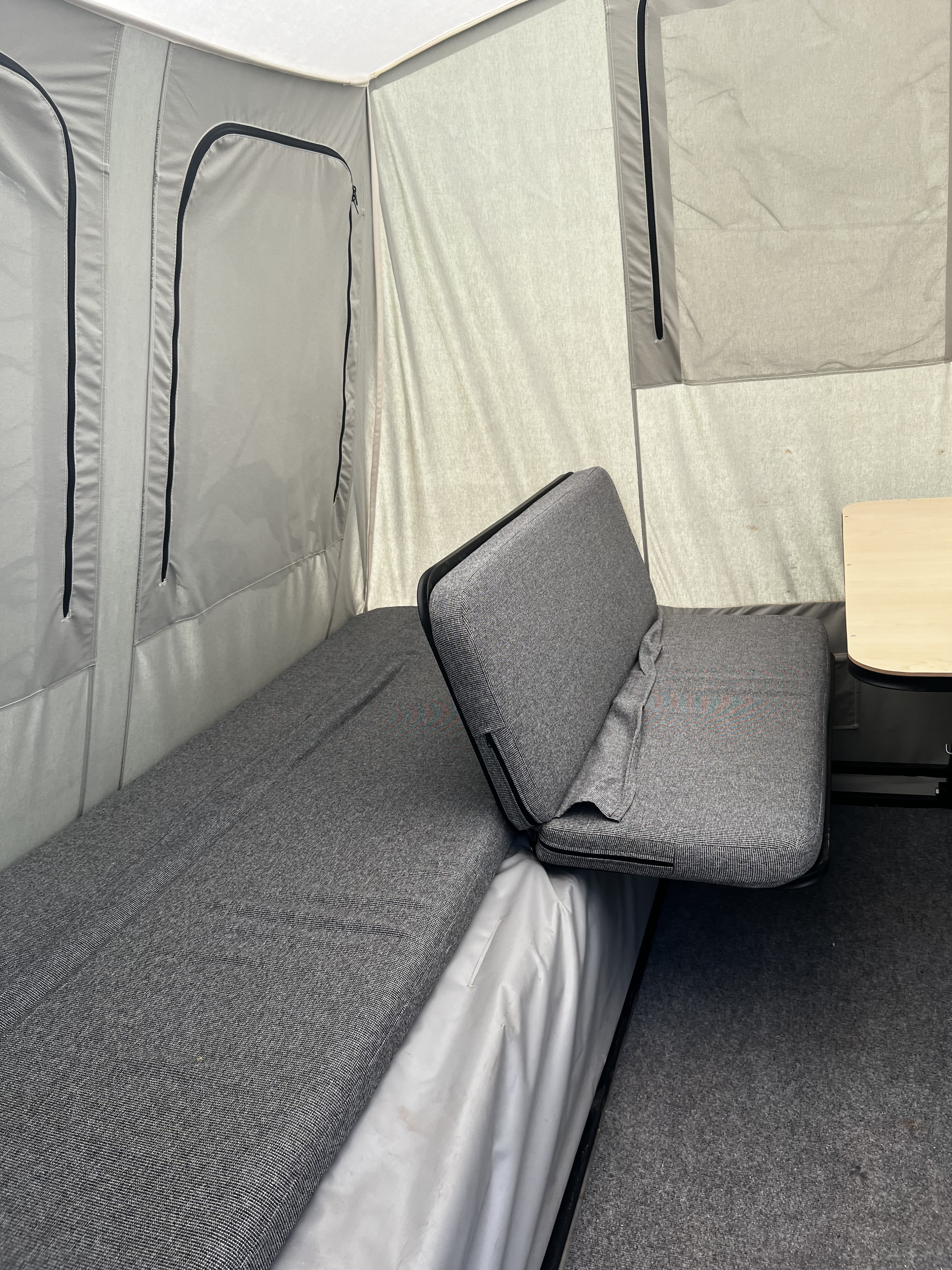 Inside an RV rental: a comfortable gray bed, dinette seating, and a table in a bright, fabric-lined space.. Jumping Jack Standard 6x8 2018