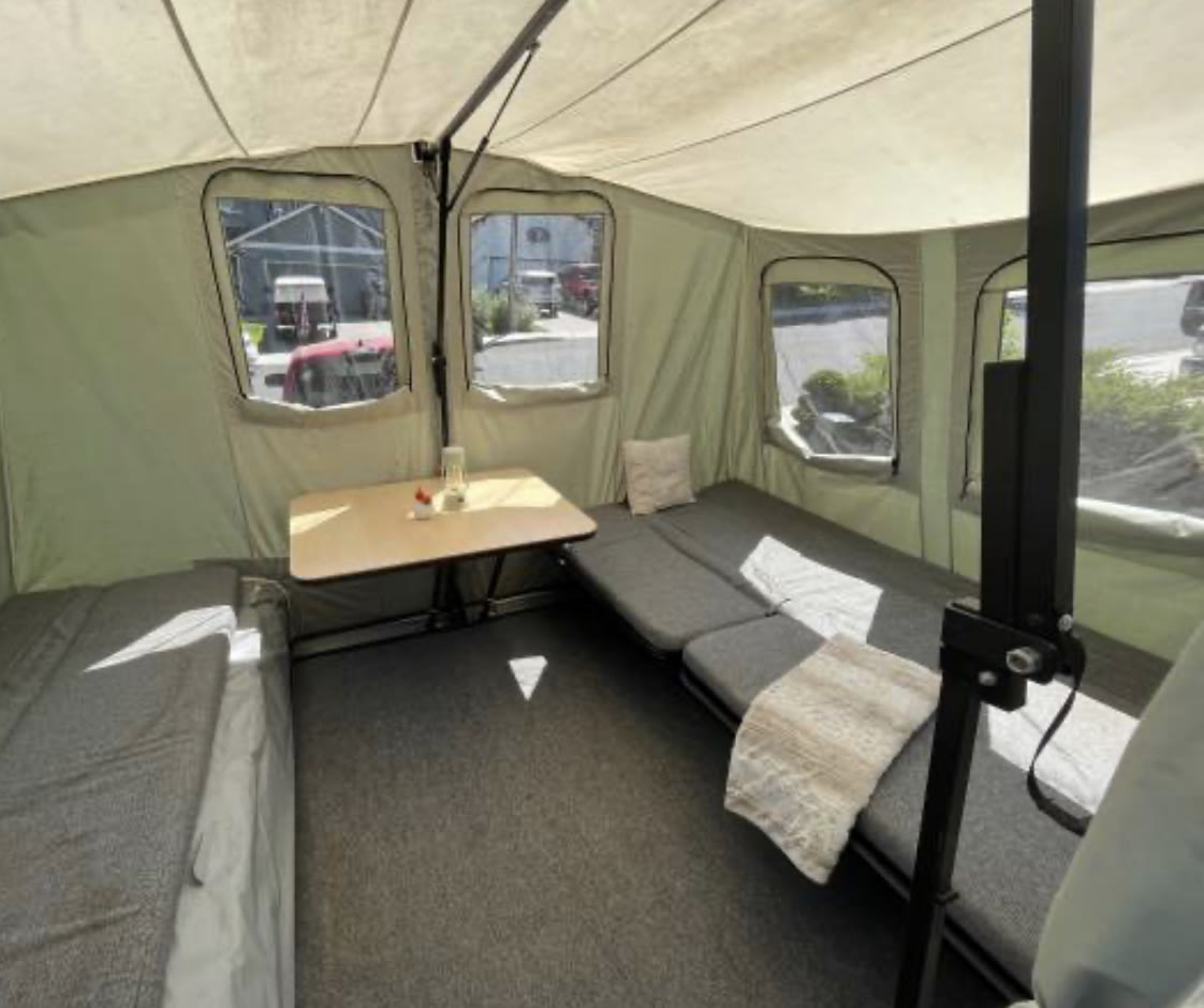 Step inside this versatile RV rental pop-up camper, featuring a cozy seating area, table, and large windows for scenic views.. Jumping Jack Standard 6x8 2018