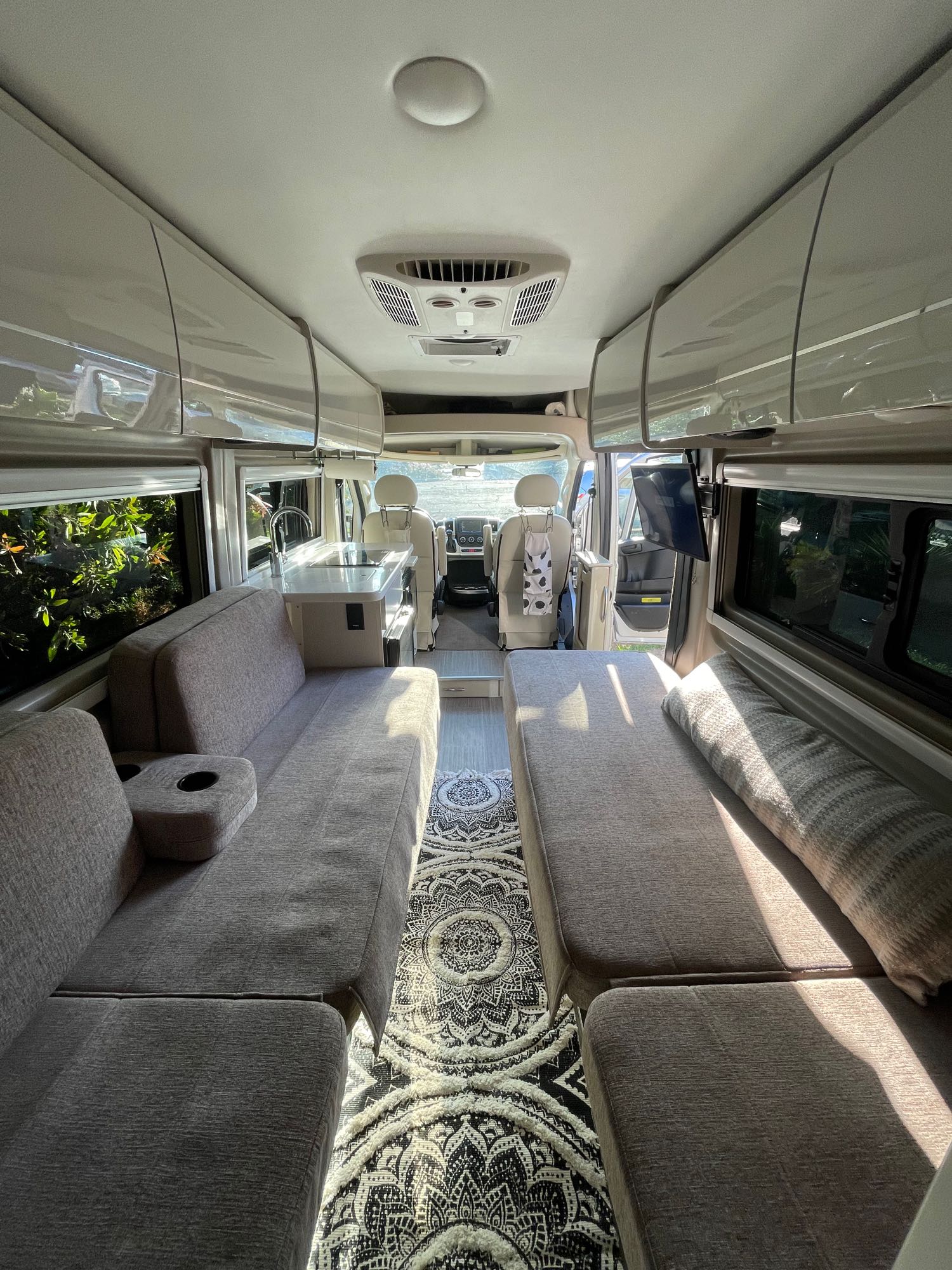 Modern rv rental interior showing a cozy living space with seating/beds, compact kitchenette, and overhead storage.. Thor Tellaro 2021