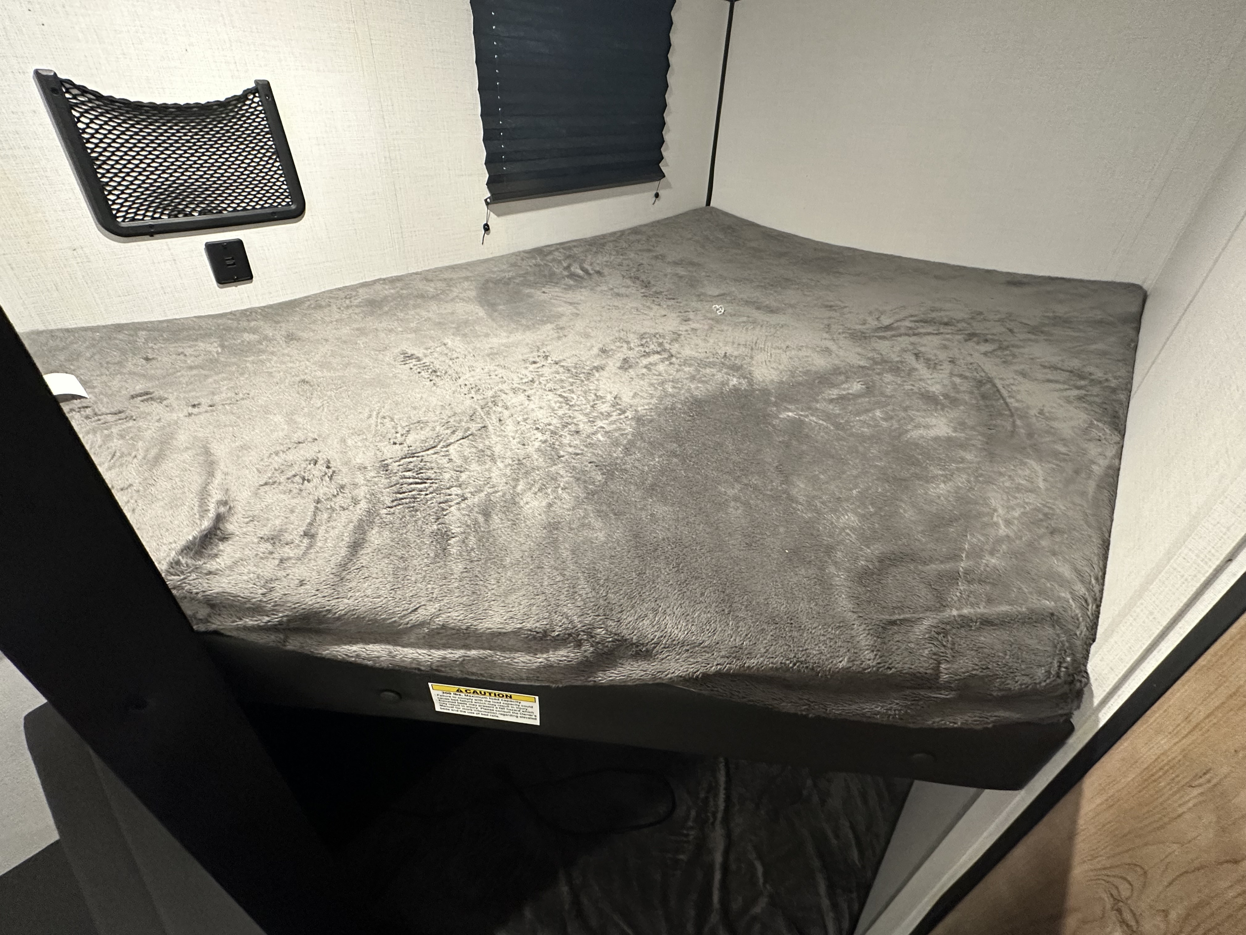 Cozy RV rental bunk bed features soft grey bedding, mesh storage, and a blackout blind, ready for comfortable rest.. Keystone RV Springdale 2023