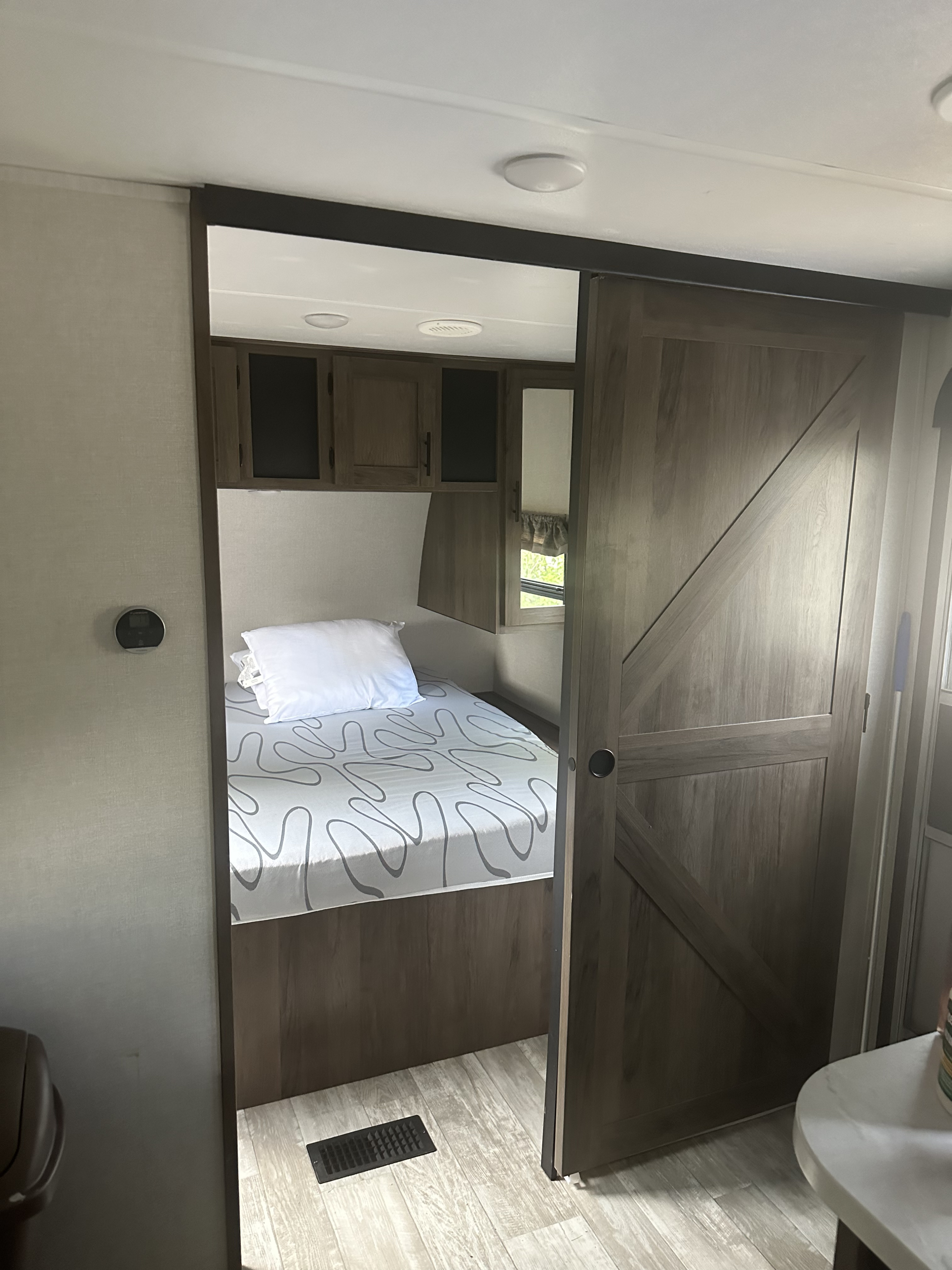 Compact RV rental bedroom with a cozy bed, overhead cabinets, and a stylish sliding barn door, offering a comfortable interior.. Avenger Avenger Trailer 2021