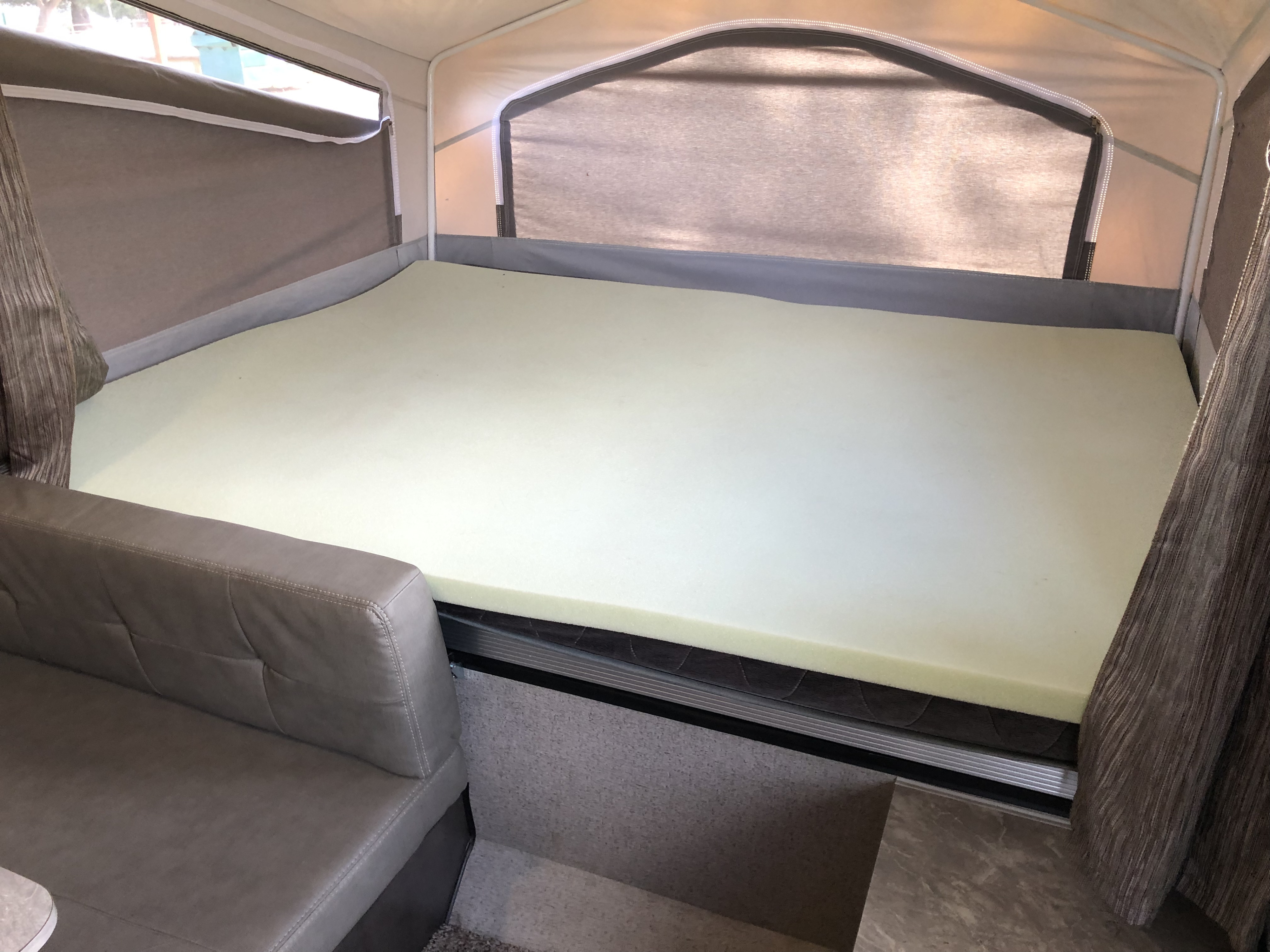 Comfortable RV rental interior: view of a bed with a foam topper, fabric walls, and sofa inside a pop-up camper.. Forest River Rockwood Freedom 2020