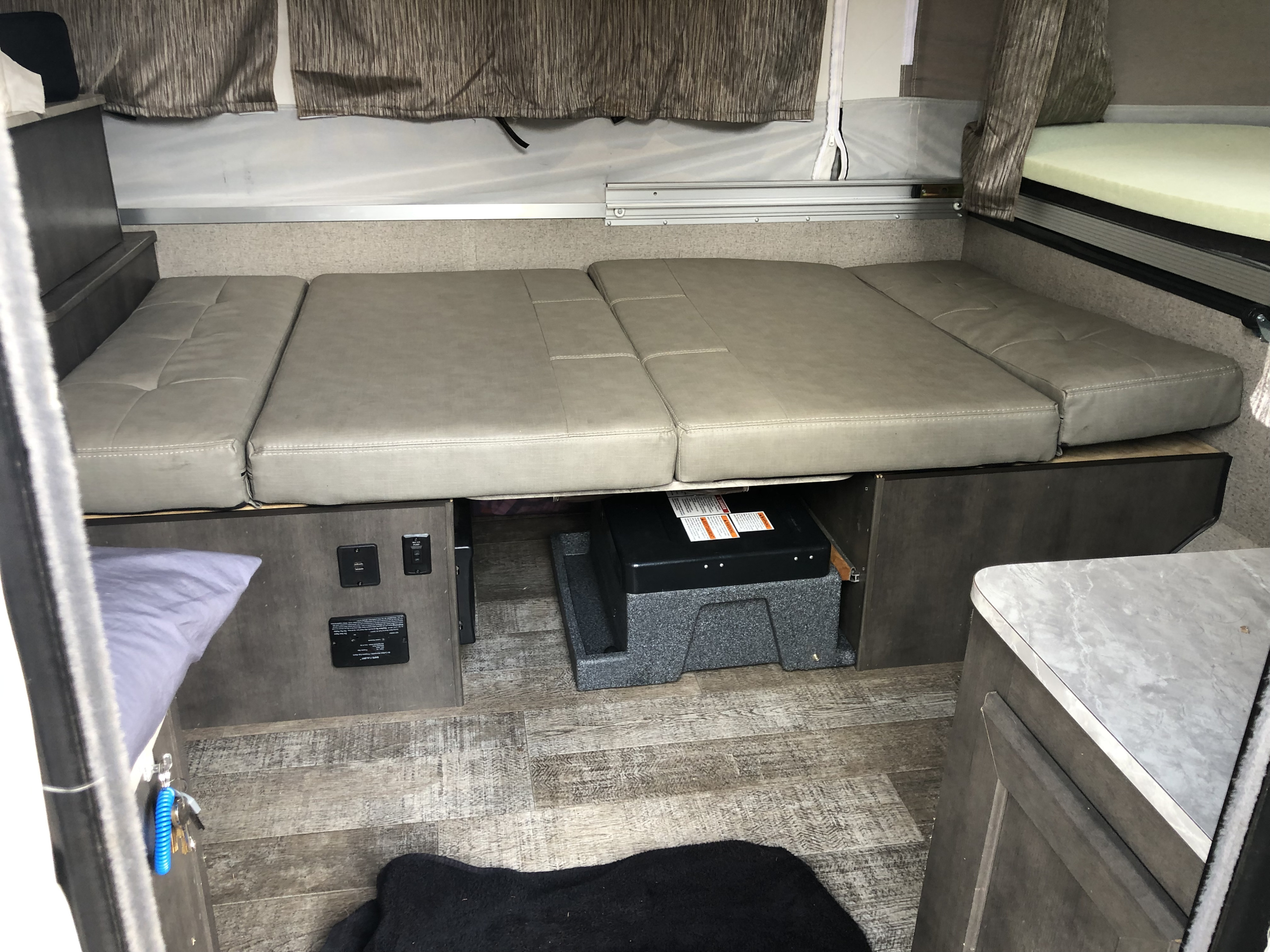 Spacious RV rental interior featuring gray convertible bench seating, under-seat storage, and a pop-up bunk bed above, ideal for travel.. Forest River Rockwood Freedom 2020