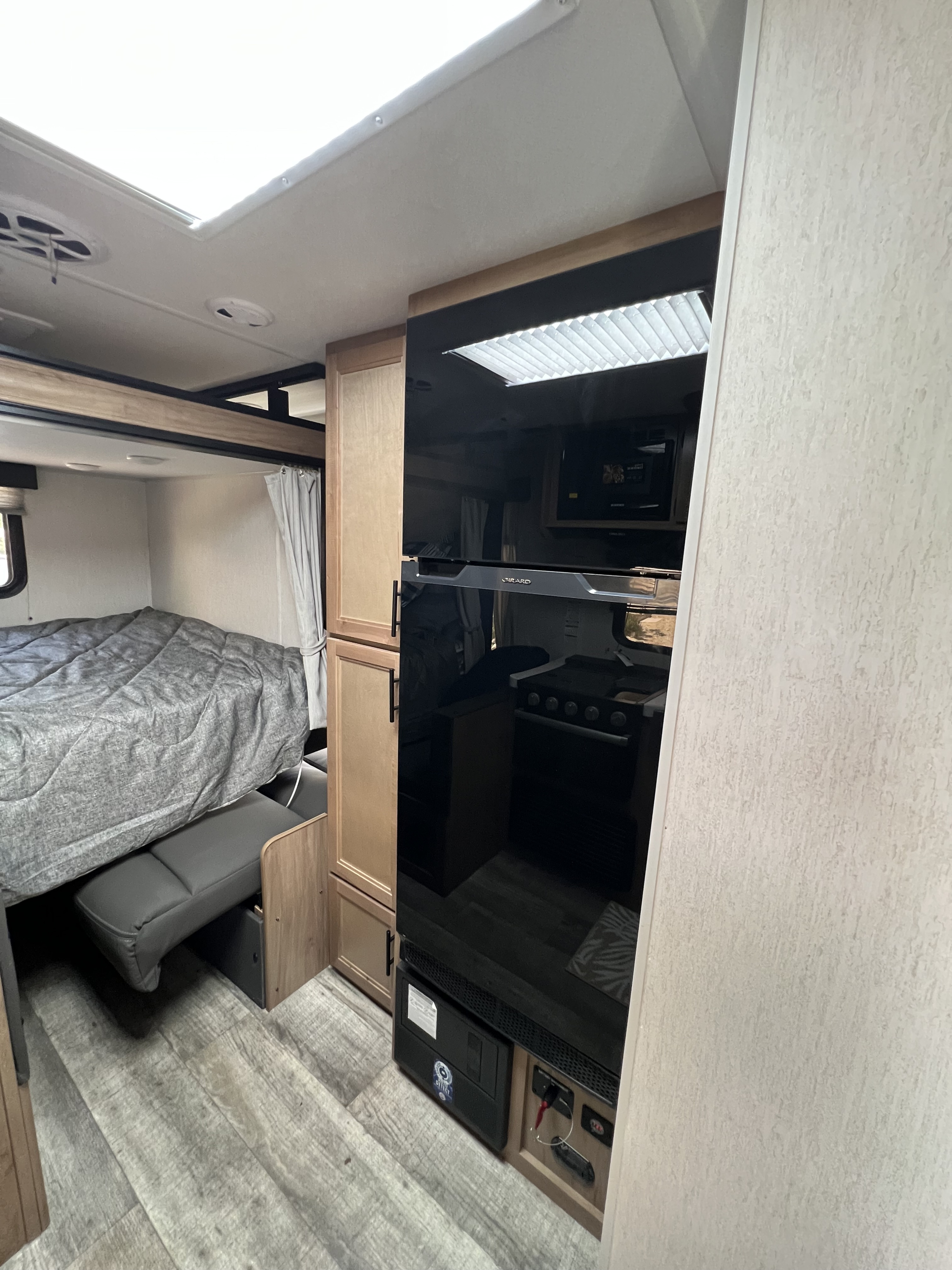 Cozy RV rental interior with a comfortable bed, pull-out bench, modern black refrigerator, and wood cabinets.. Forest River Cherokee  Grey Wolf 19SM 2023
