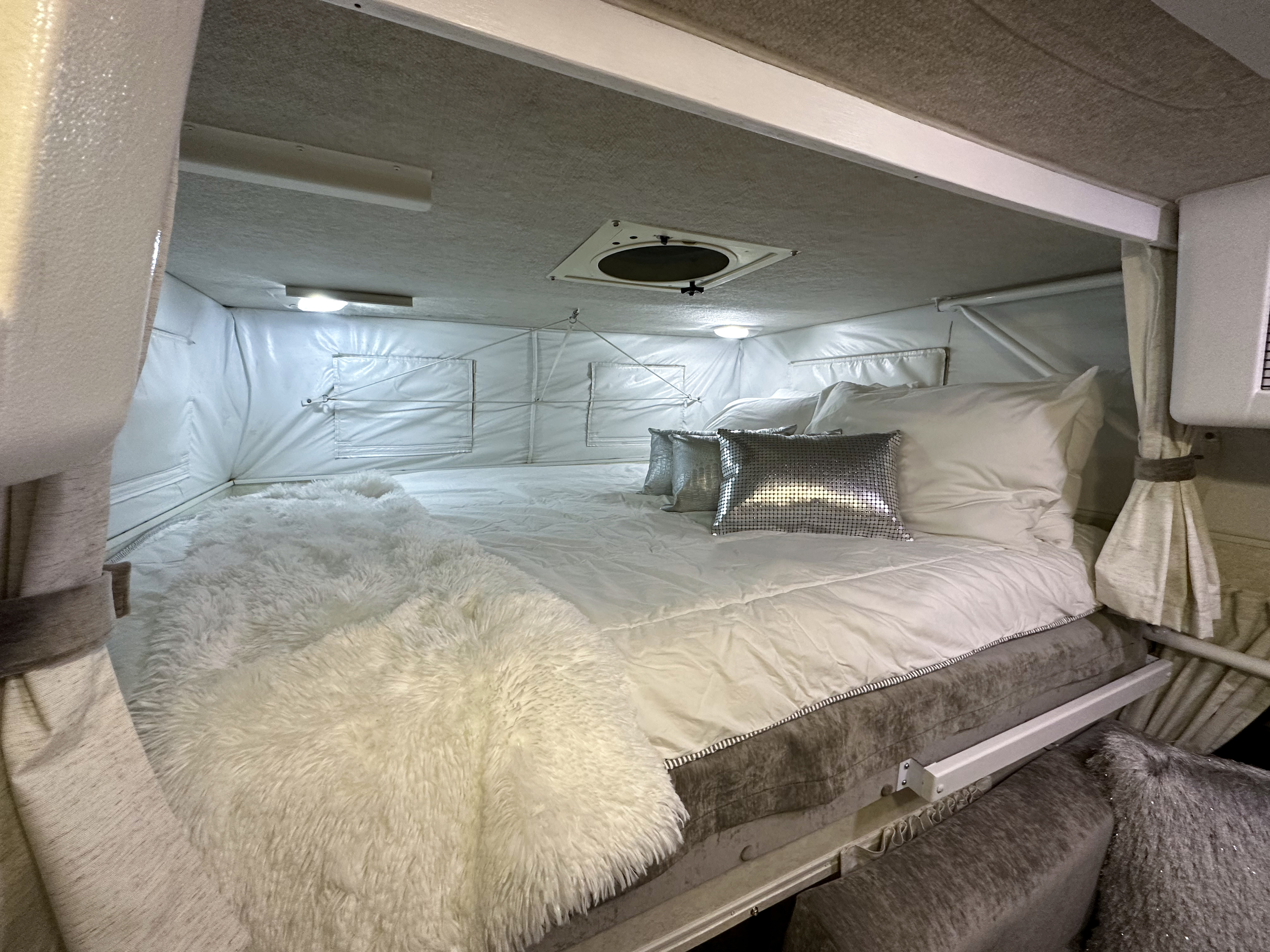 Cozy RV rental bed area featuring white linens, a fluffy throw, and modern interior details.. Hallmark Everest 2011