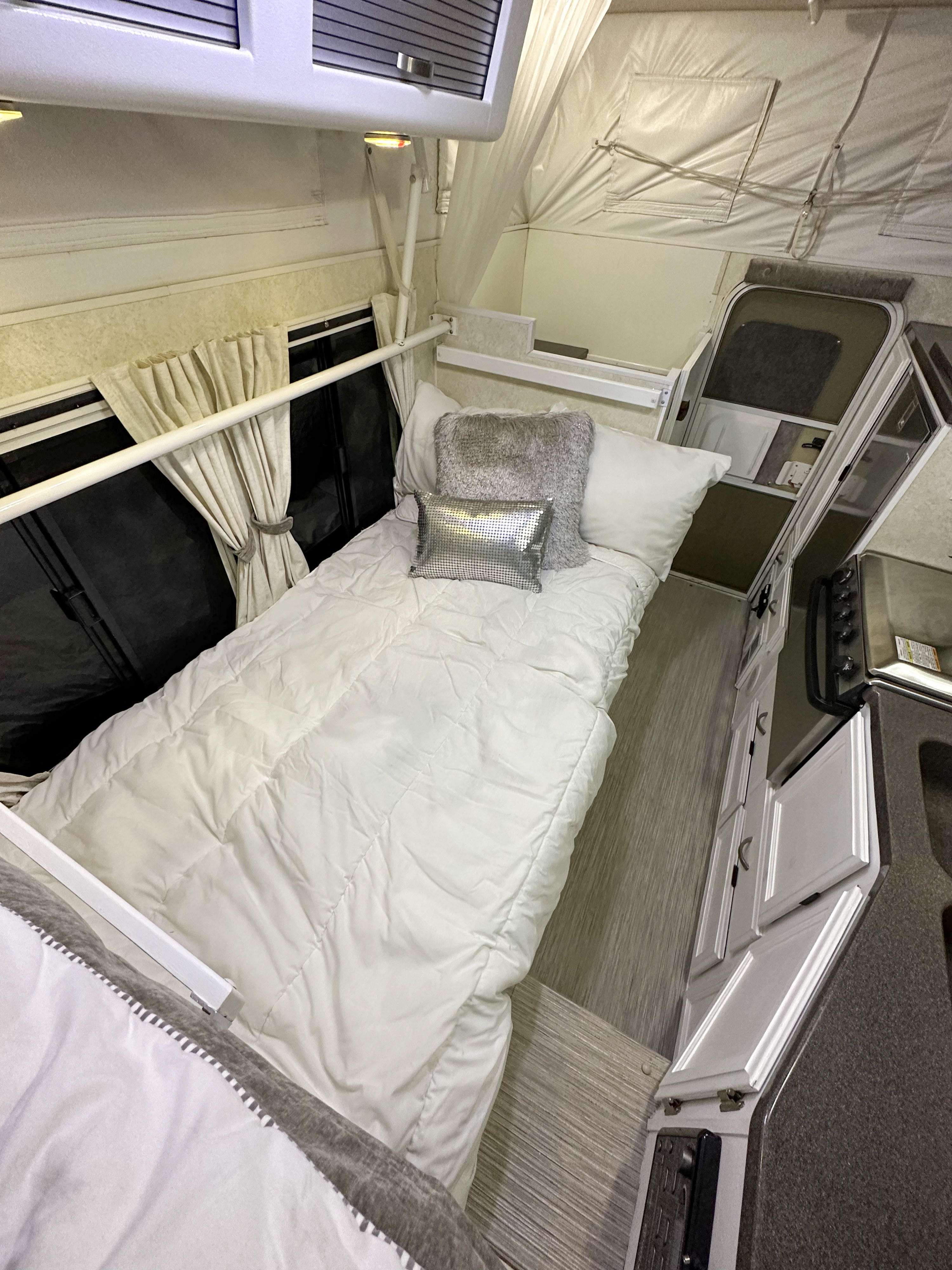 Cozy RV rental interior, showing a bed with pillows, kitchen area, and pop-up camper design.. Hallmark Everest 2011