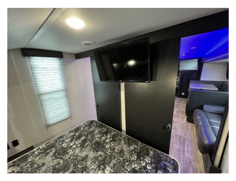 RV rental interior with a sleeping area, mounted TV, and a dinette in the rear featuring blue lights.. Forest River Cherokee Grey Wolf 2022