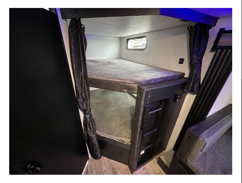 Inside an RV rental: a compact sleeping area with two bunk beds, a ladder, and privacy curtains.. Forest River Cherokee Grey Wolf 2022