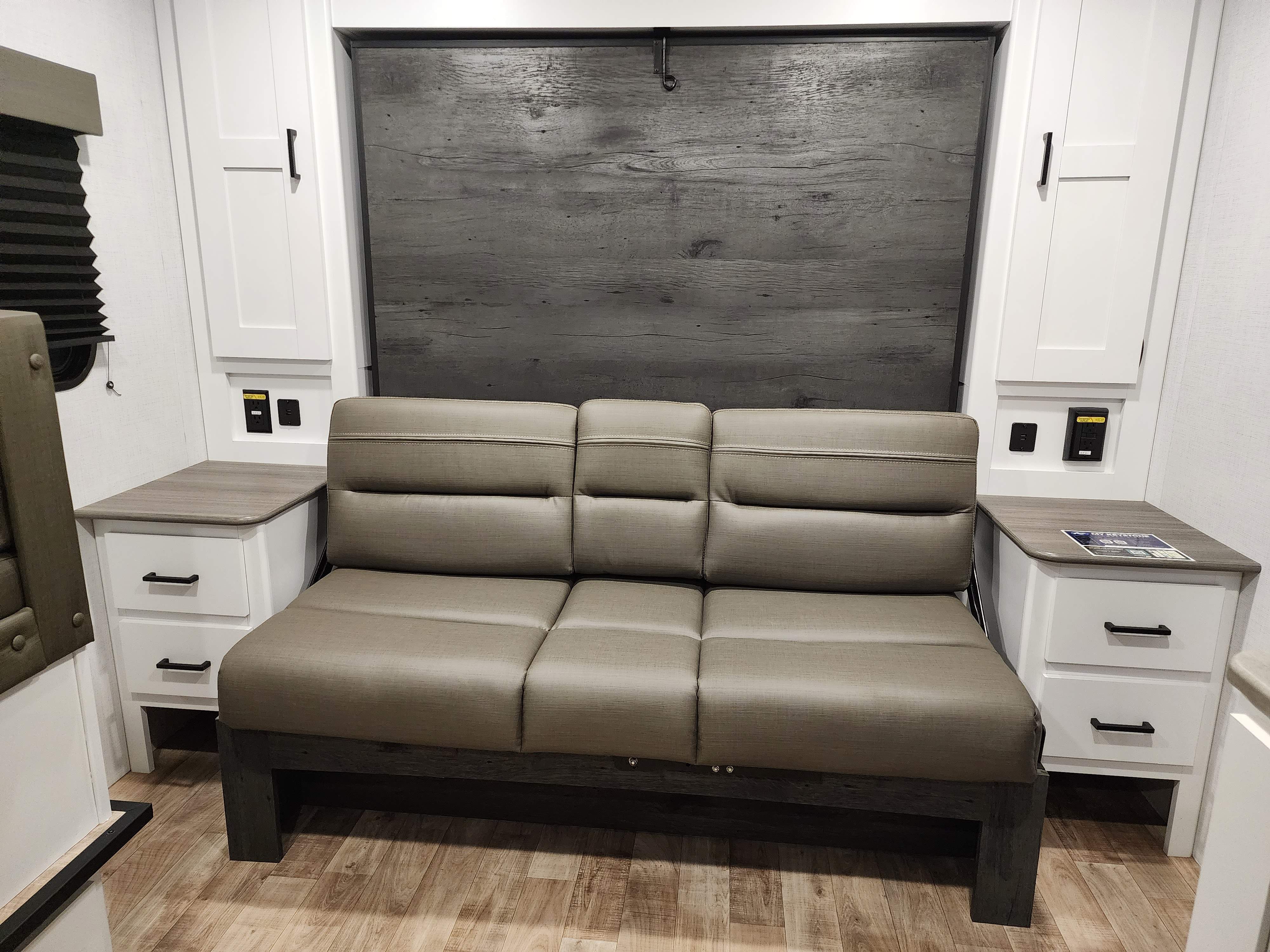 RV rental: This RV interior features a tan sofa, side storage, and a dark wood-textured wall, likely a pull-down bed.. Keystone RV Hideout 2023