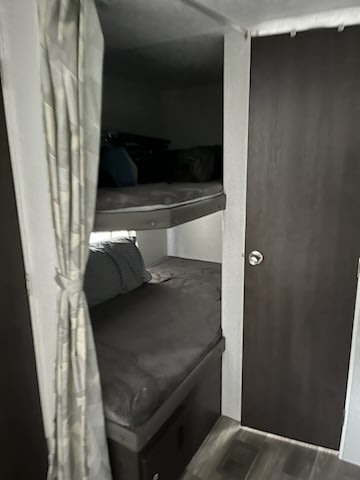 RV rental interior: Two cozy bunk beds with dark gray mattresses, a privacy curtain, and a nearby door.. Forest River Wildwood X-Lite 2020