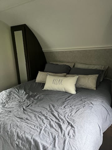 Comfortable RV rental bedroom with grey bedding and "RELAX" pillow, featuring an angled ceiling and compact design.. Forest River Wildwood X-Lite 2020