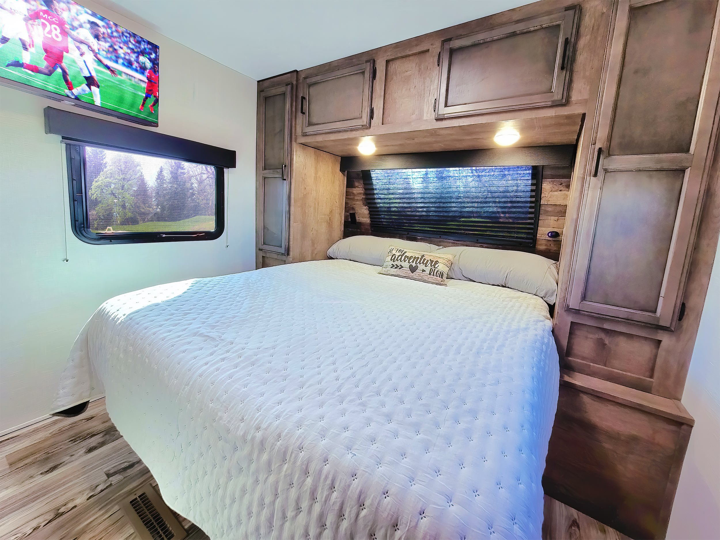 Bright RV rental bedroom featuring a large bed, TV, ample storage, and window showcasing a lush forest view.. Venture Rv Sporttrek 2022