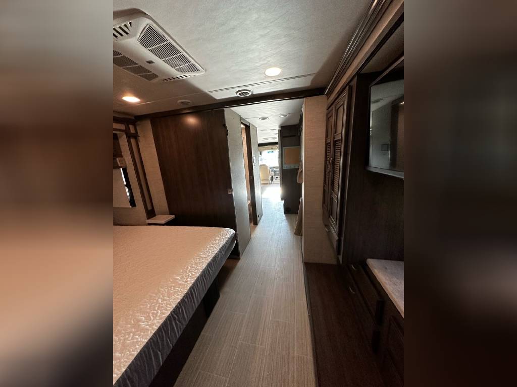 Modern RV rental interior showcasing a bedroom, central hallway, ceiling AC unit, and dark wood storage.. Other Precept 2022