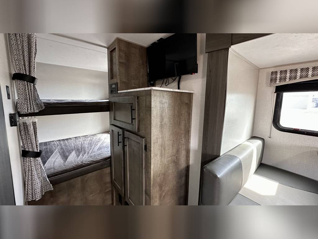 Cozy RV rental interior: bunk beds with curtains, TV, storage cabinets, and a dinette seating area by the window.. Venture Rv Sonic 2022