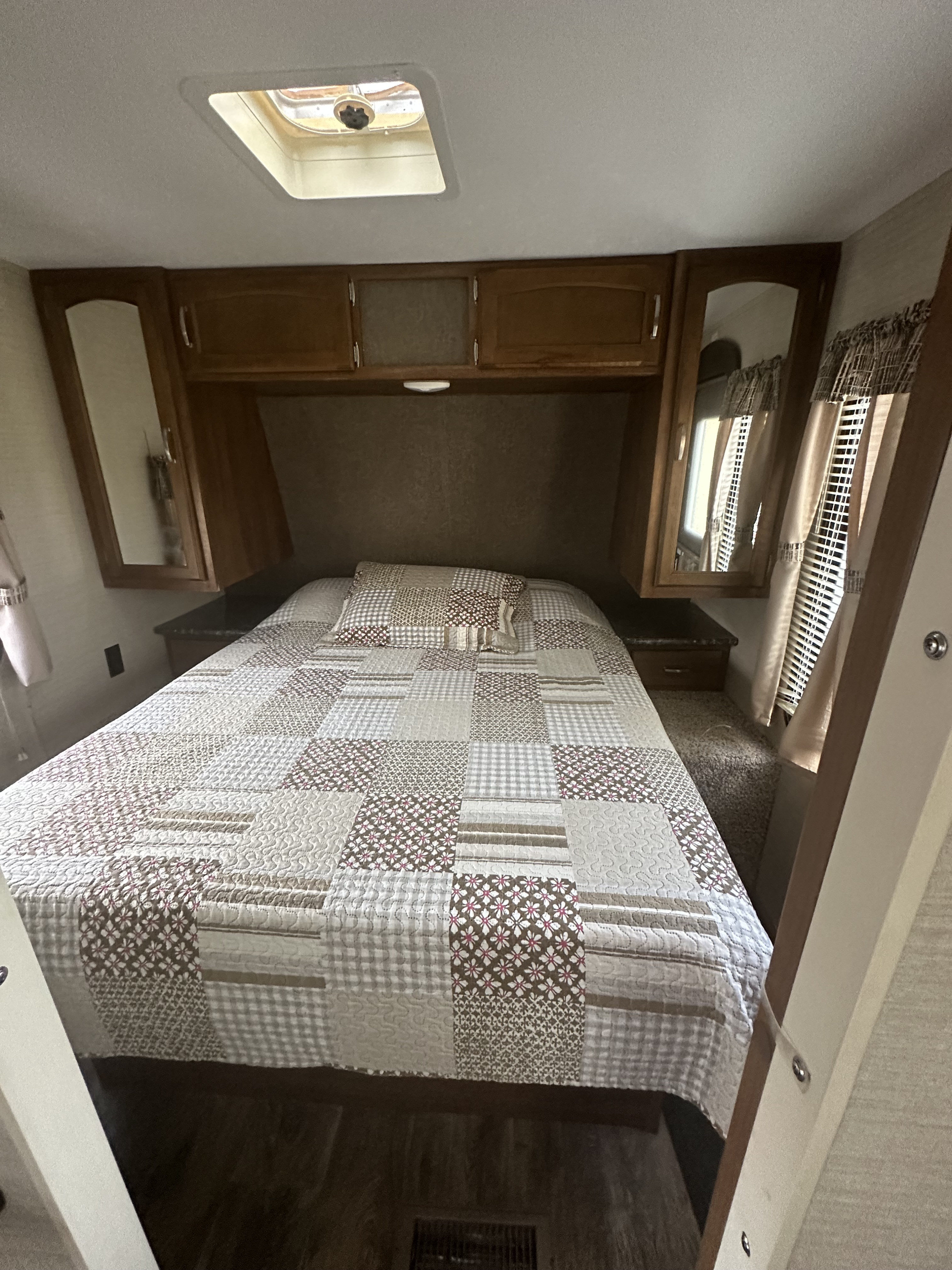 An RV rental's bedroom interior with a patterned quilt on the bed, overhead storage, and a ceiling skylight.. Keystone RV Springdale 2016