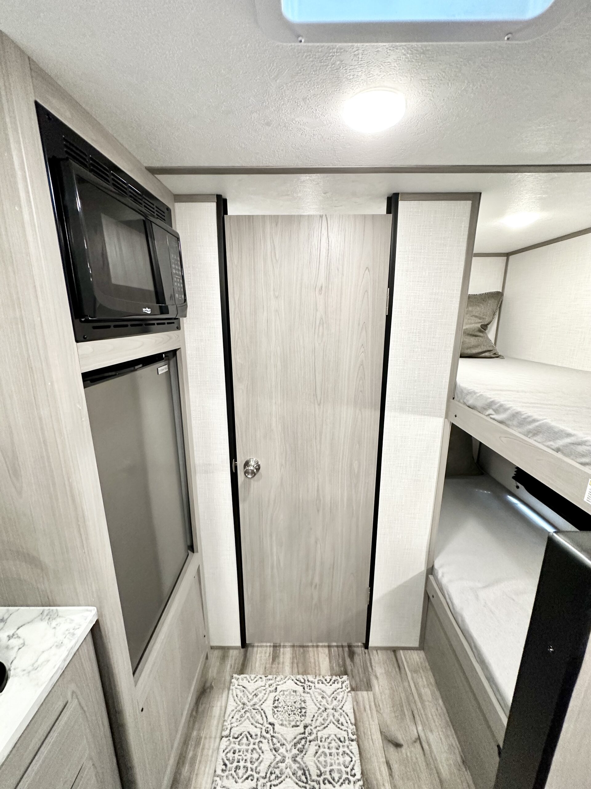 RV rental interior: compact kitchen with microwave & fridge, wooden door, and cozy bunk beds for travelers.. Coleman Lantern 17b 2023